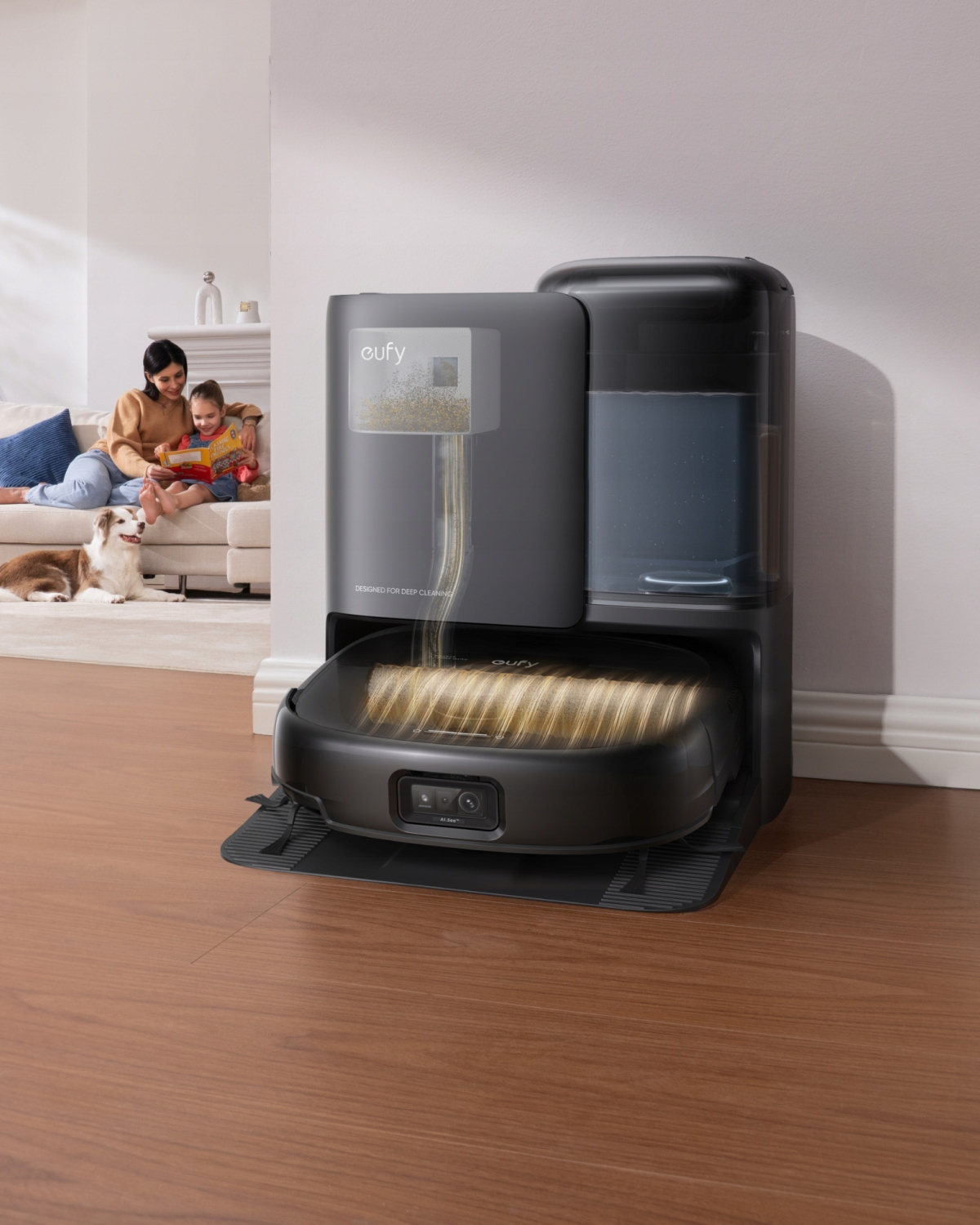 Robot odkurzający zadokowany do swojej bazy. Kobieta i dziecko widoczne w tle.