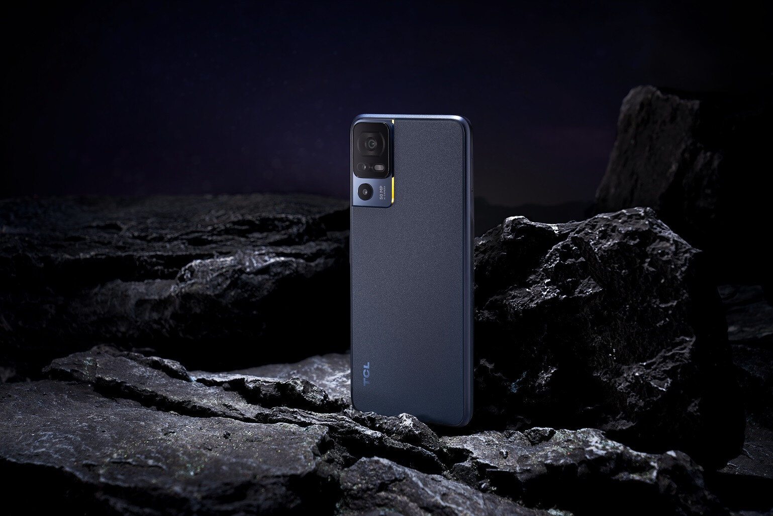 Un teléfono TCL azul oscuro sobre una superficie rocosa con un fondo estrellado. El teléfono está boca arriba.