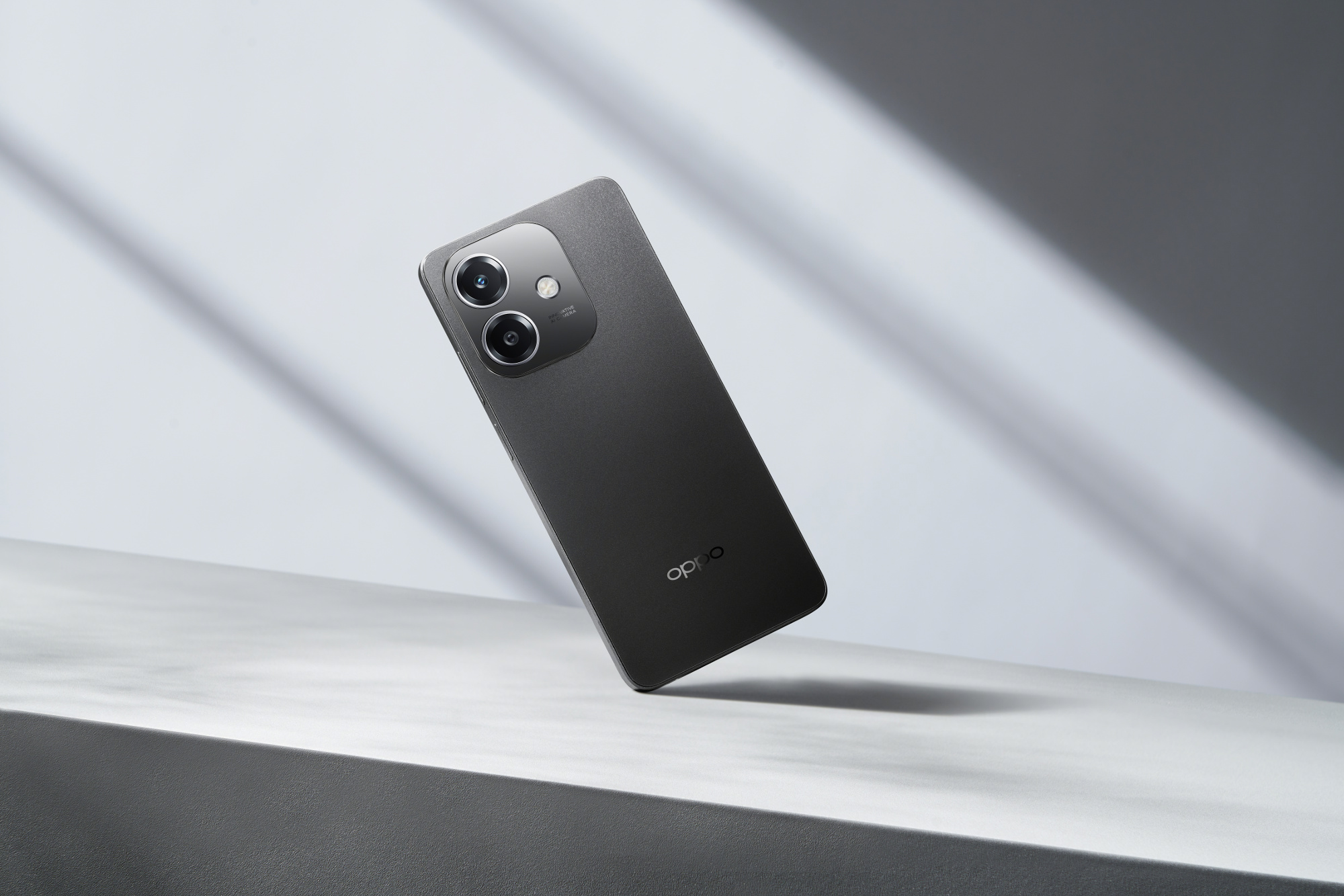 Un teléfono gris oscuro con dos cámaras sobre una superficie blanca con sombras. El logotipo de Oppo es visible.