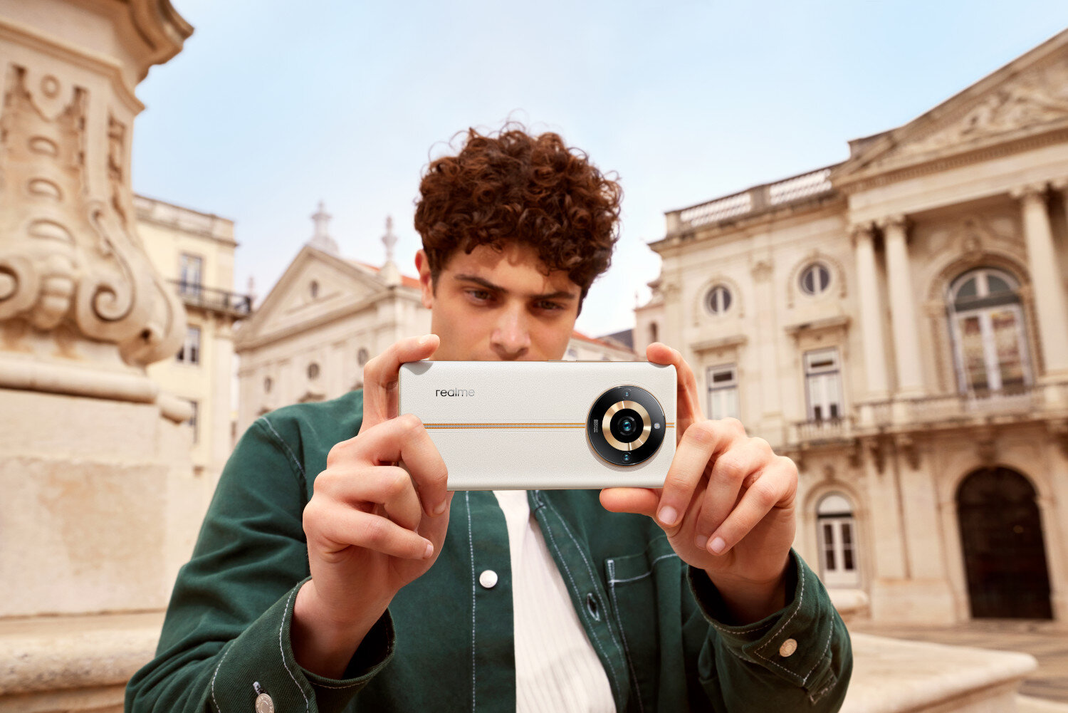 Uomo che tiene un telefono davanti a un edificio. Il telefono è bianco, ha tre fotocamere.