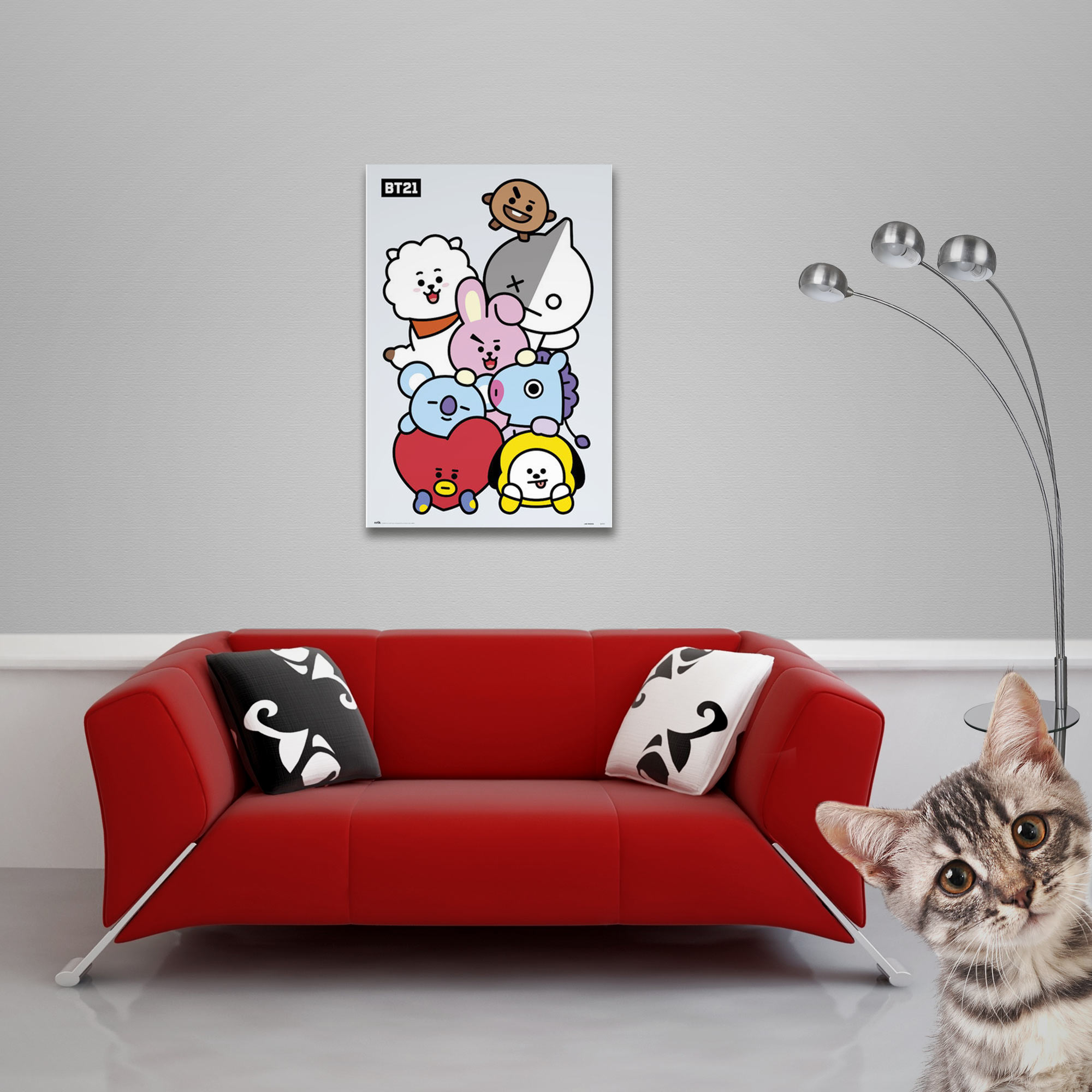 Ein Poster mit BT21-Charakteren an einer grauen Wand, ein rotes Sofa und eine Katze im Vordergrund.