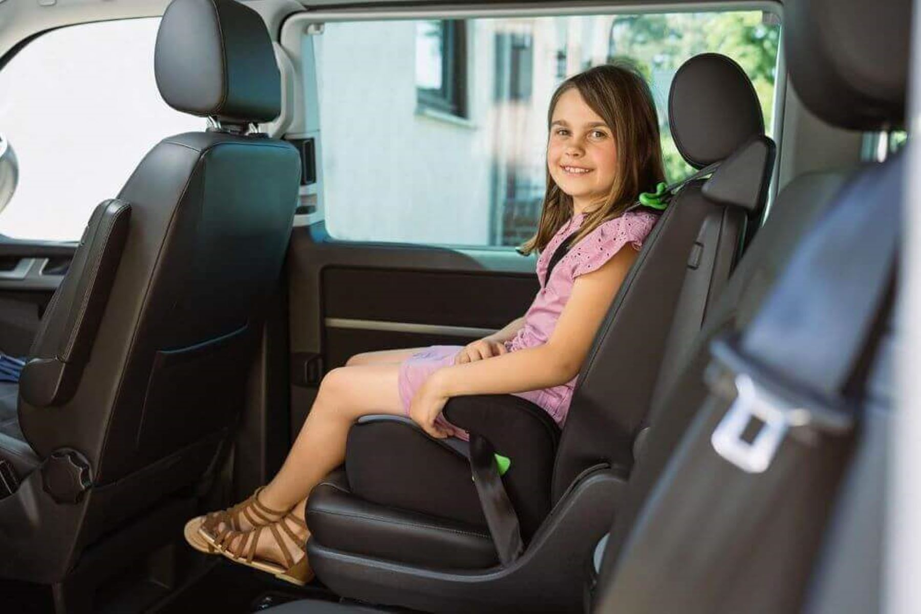 Ein Mädchen sitzt in einem Autositz in einem Fahrzeug und lächelt in die Kamera.
