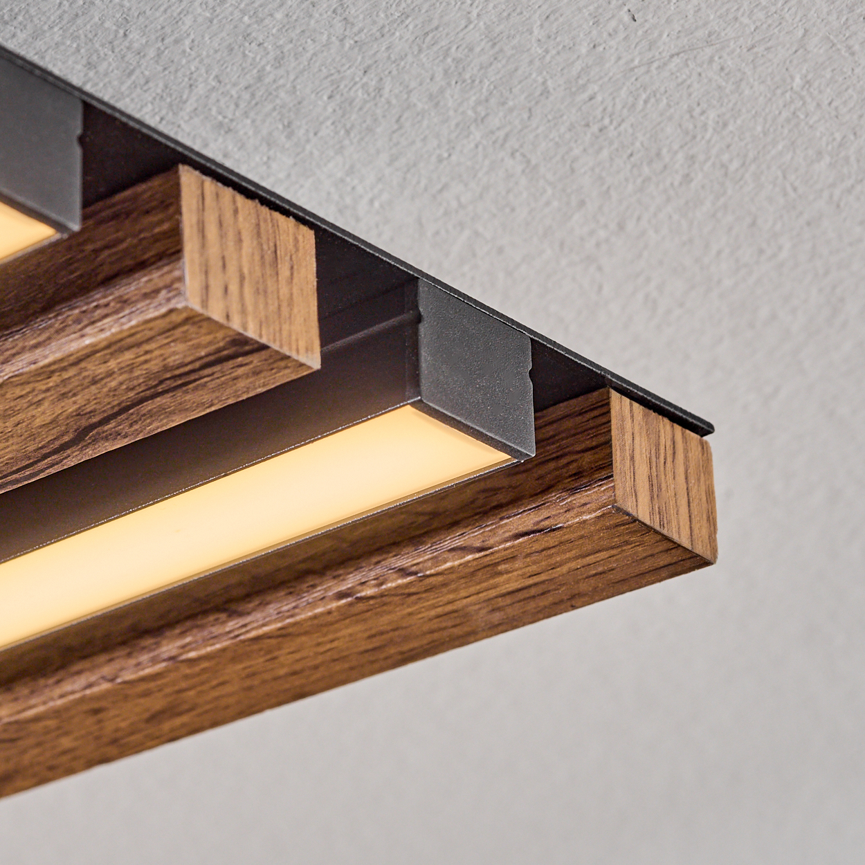 Nahaufnahme einer Deckenleuchte mit Holzbalken, schwarzen Akzenten und weißem Licht. Weiße Decke.