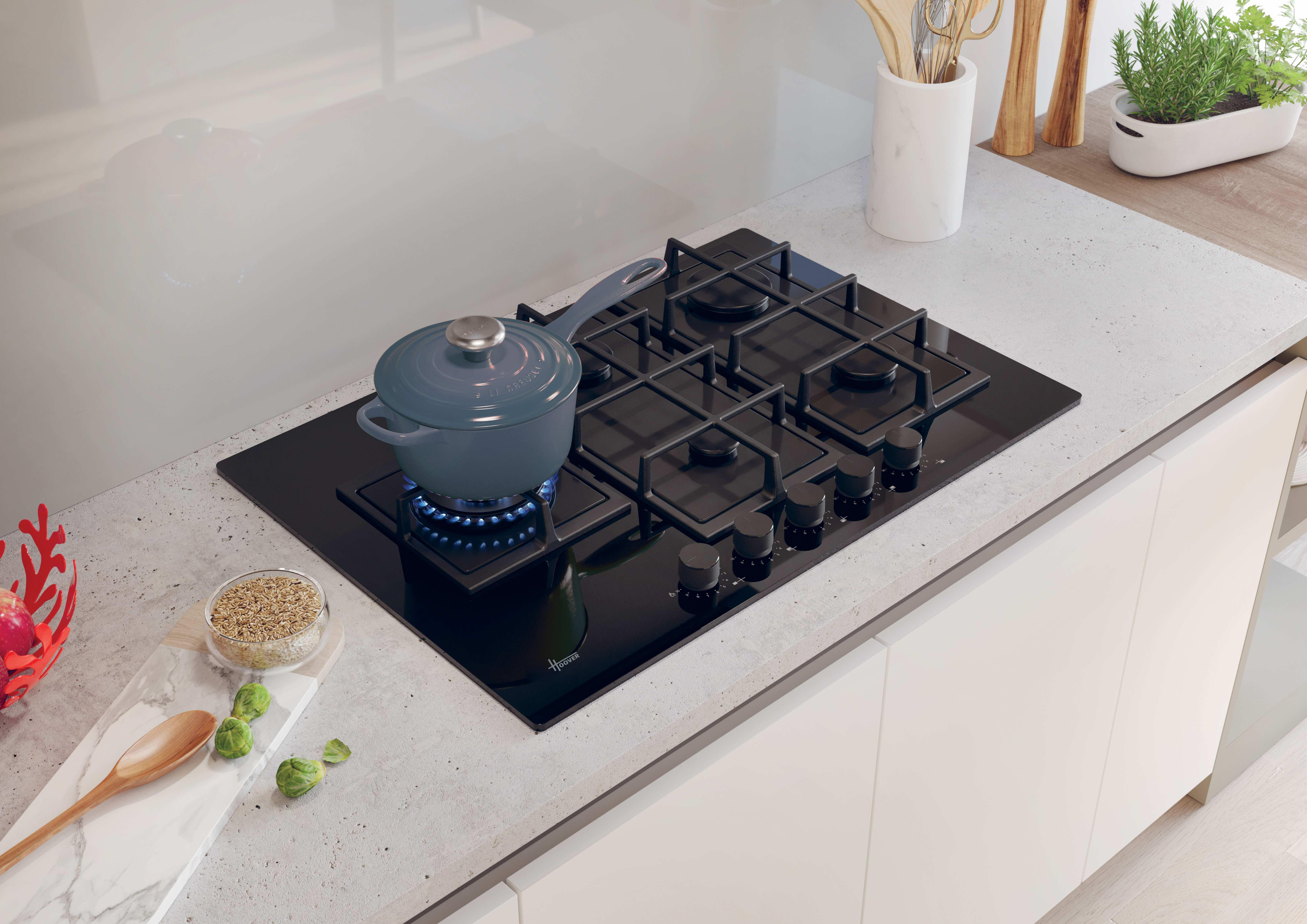 Un piano cottura con una pentola blu su un bruciatore acceso, con altri oggetti da cucina sul piano di lavoro.