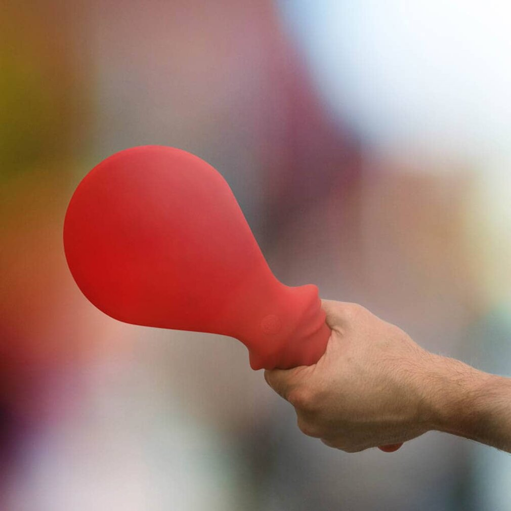 Dłoń trzymająca czerwoną zabawkę erotyczną w kształcie łzy. Tło jest rozmyte.