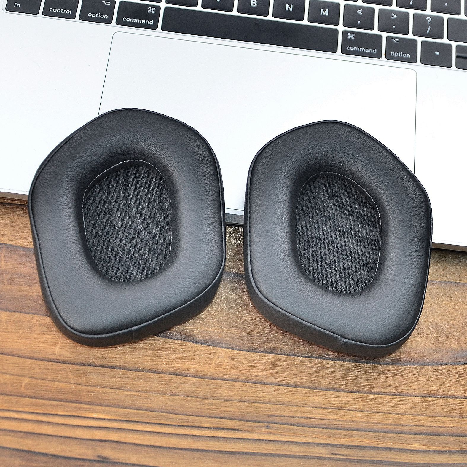 Due cuscinetti auricolari neri per cuffie posizionati su una superficie in legno vicino alla tastiera di un laptop.