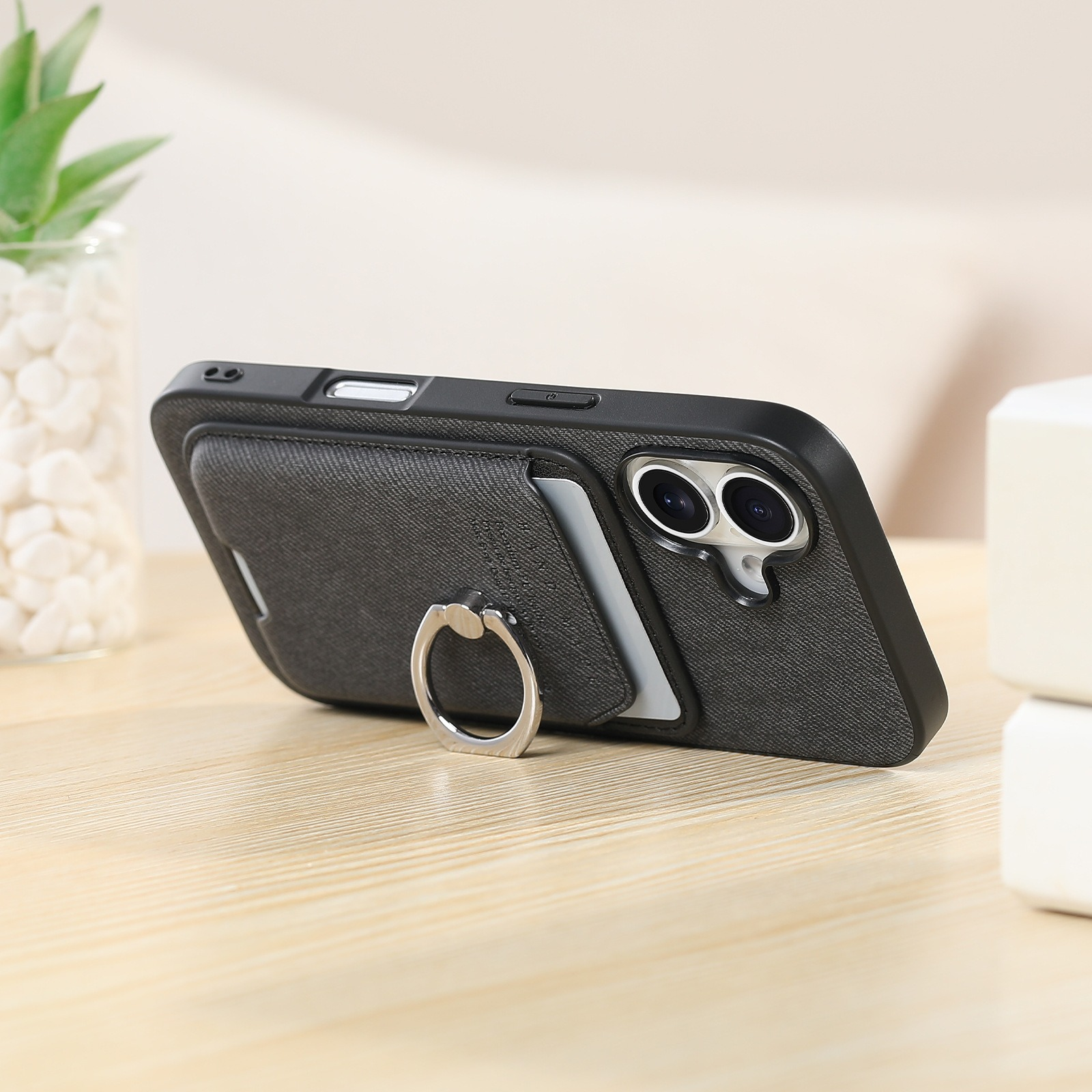 Custodia per telefono nera con anello, appoggiata su legno. Un bicchiere sullo sfondo.