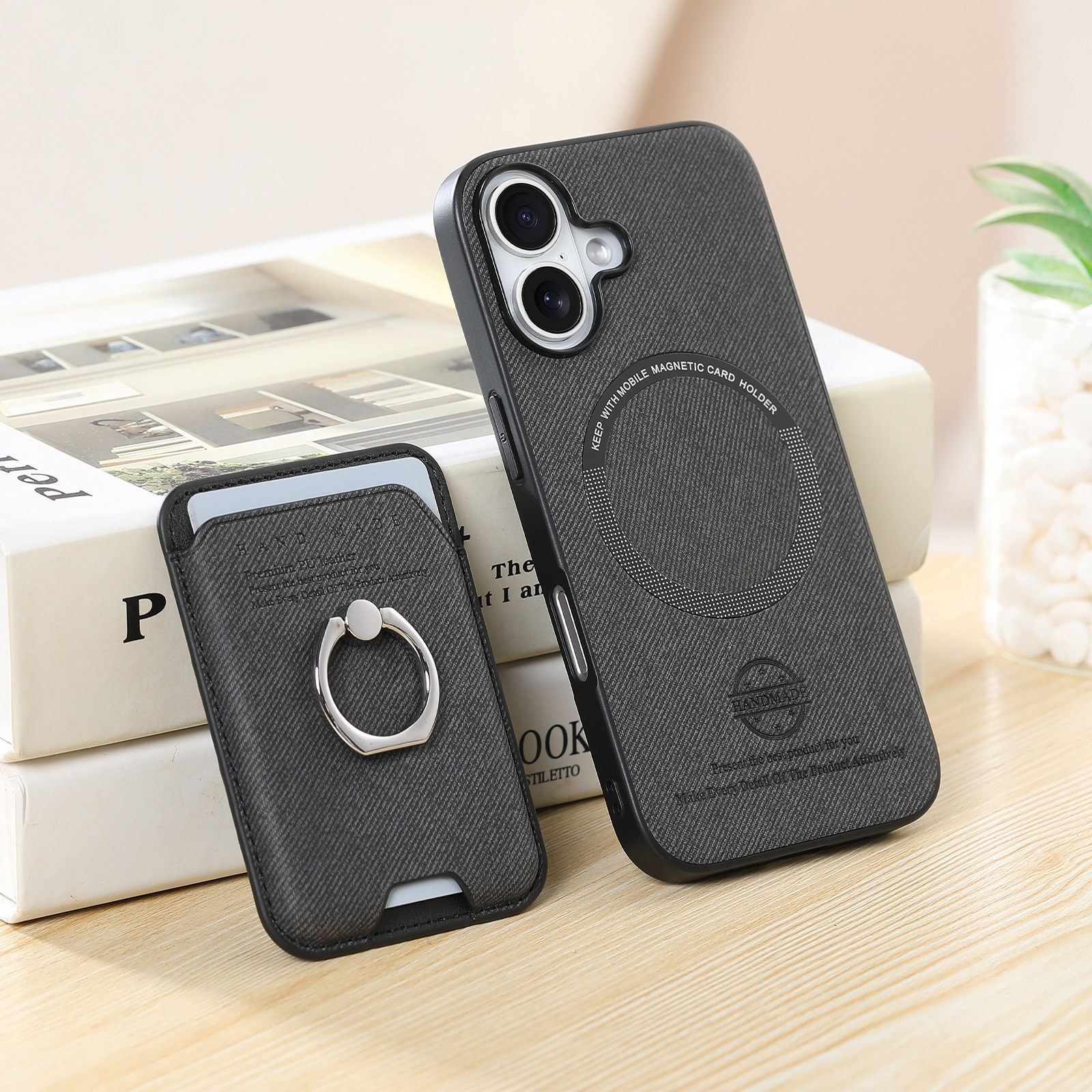 Custodia per telefono nera con anello e porta carte. Libri e una piccola pianta sullo sfondo.