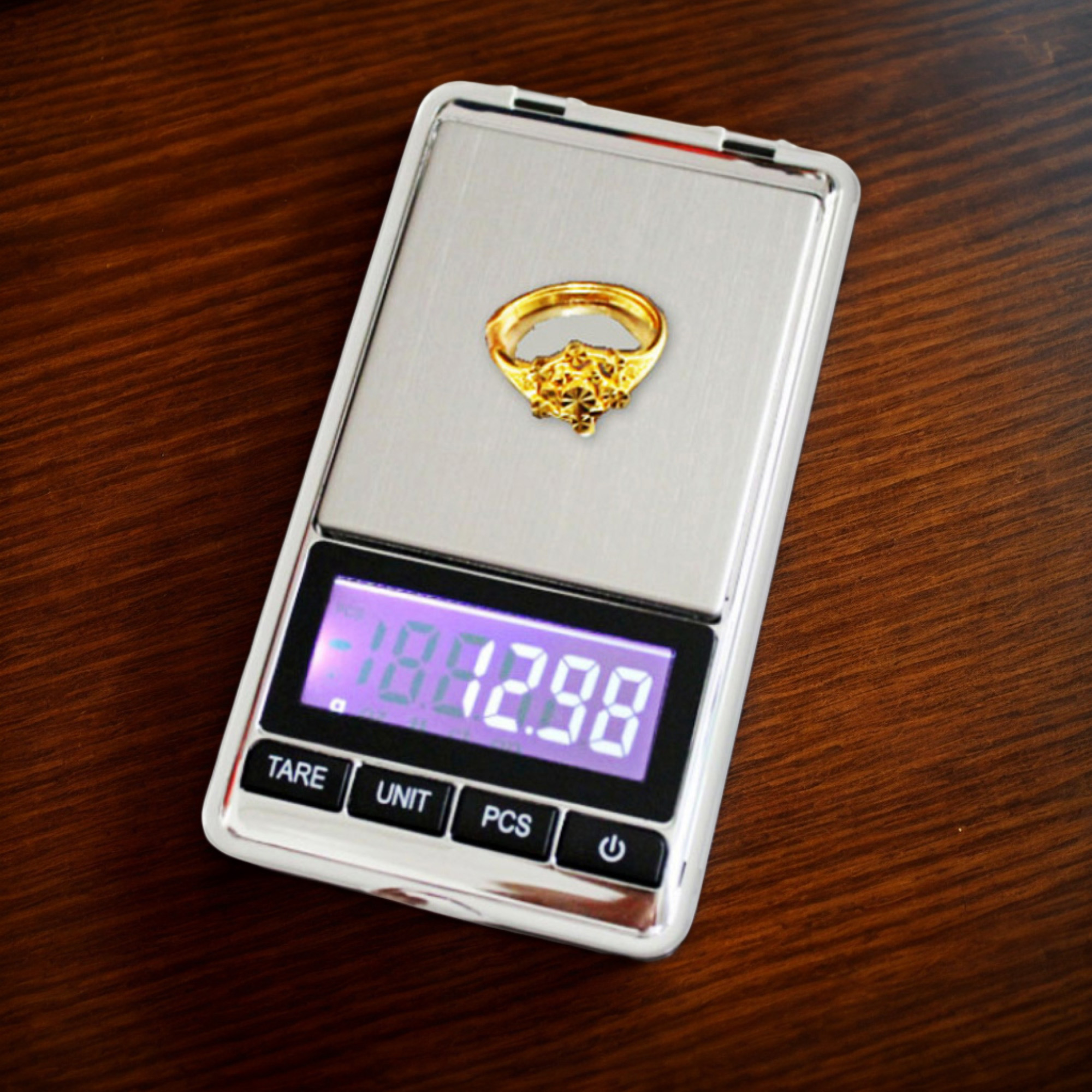 Eine kleine Digitalwaage mit einem Goldring darauf. Das Display zeigt ein Gewicht an.
