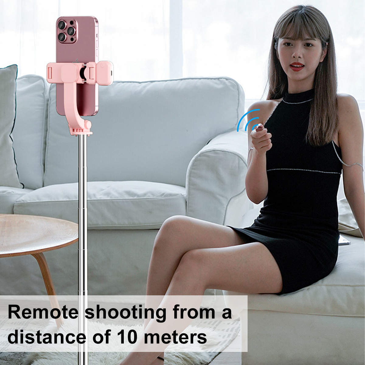 Eine Frau benutzt einen pinken Telefonhalter an einem Selfie-Stick, sitzt auf einem Sofa.