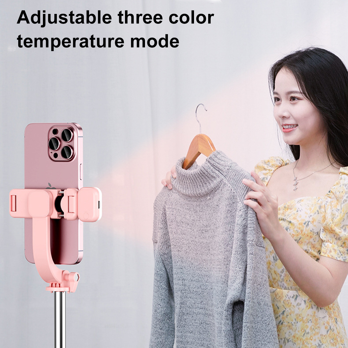 Eine Frau hält einen Pullover in der Nähe eines Telefons, das an einem Selfie-Stick befestigt ist. Es hat einen rosa Halter und eine silberne Stange.