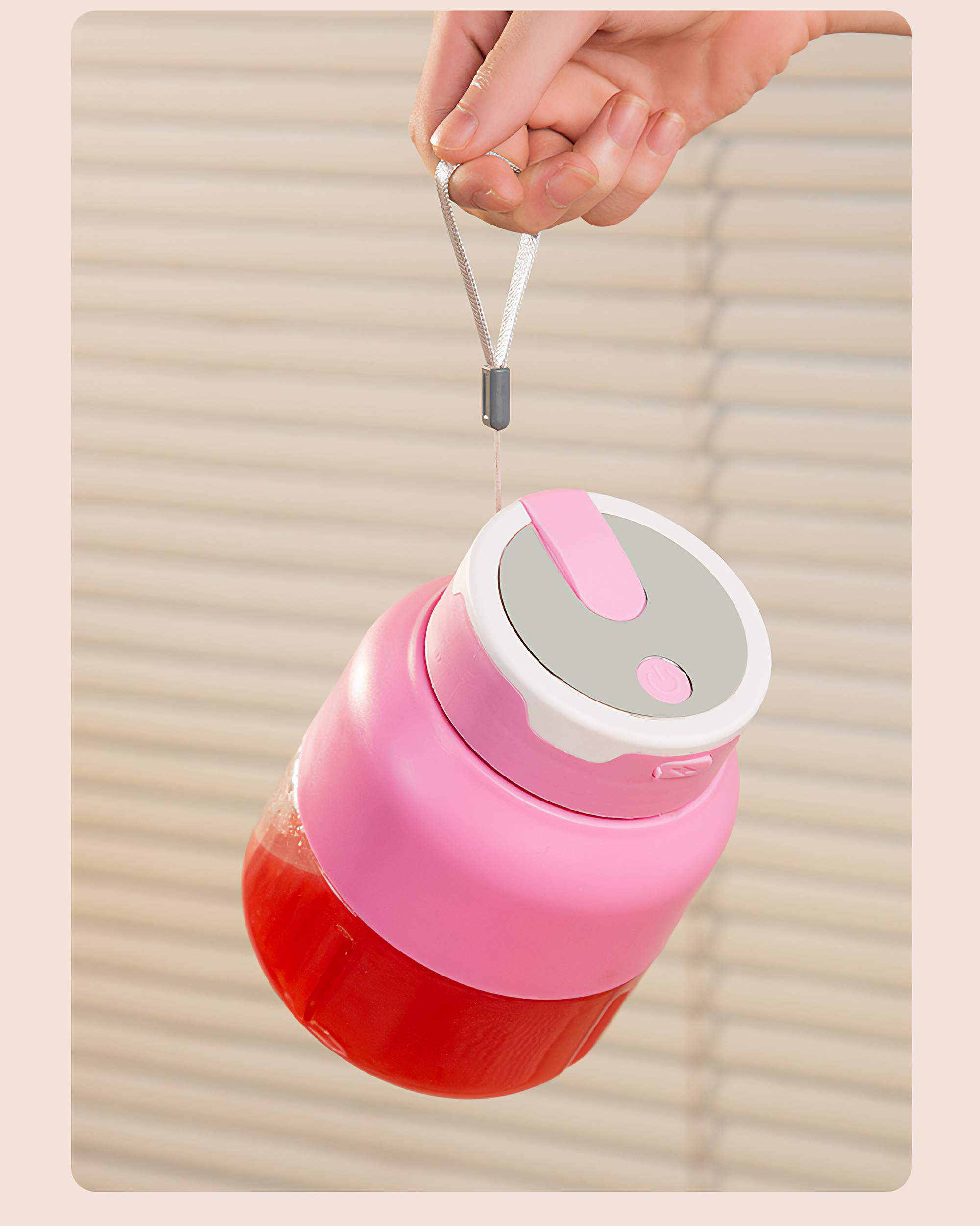 Hand hält einen pinkfarbenen tragbaren Mixer. Der Mixer ist mit roter Flüssigkeit gefüllt. Ein Faden ist am Deckel befestigt.