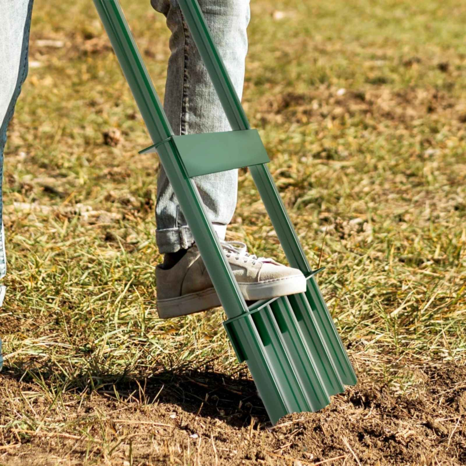 Person benutzt ein grünes Gartengerät. Das Werkzeug wird in den Boden gesteckt. Gras Hintergrund.