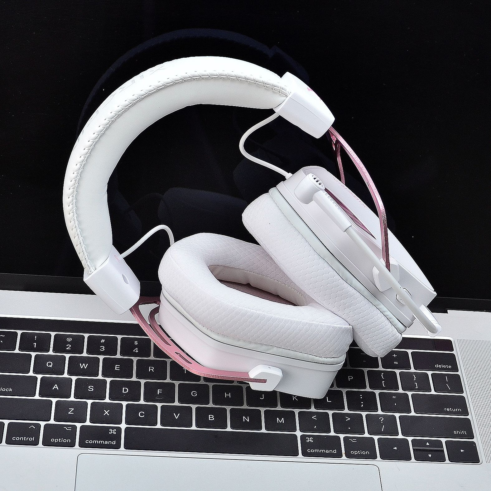Cuffie bianche con microfono su una tastiera di un laptop. Le cuffie sono bianche con dettagli rosa.