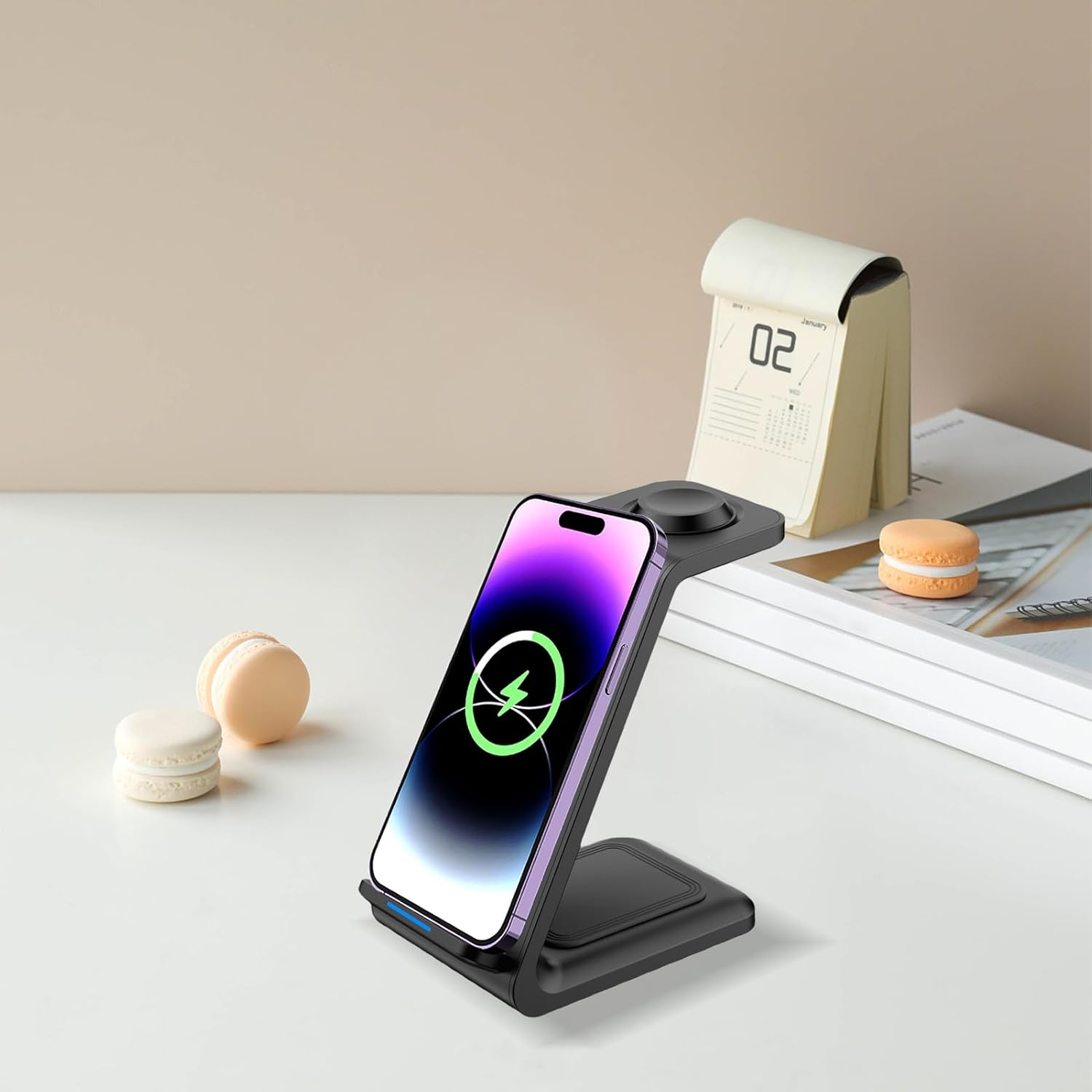 Ein Telefon wird drahtlos auf einem schwarzen Ständer aufgeladen, neben Macarons und einem Kalender mit 02.
