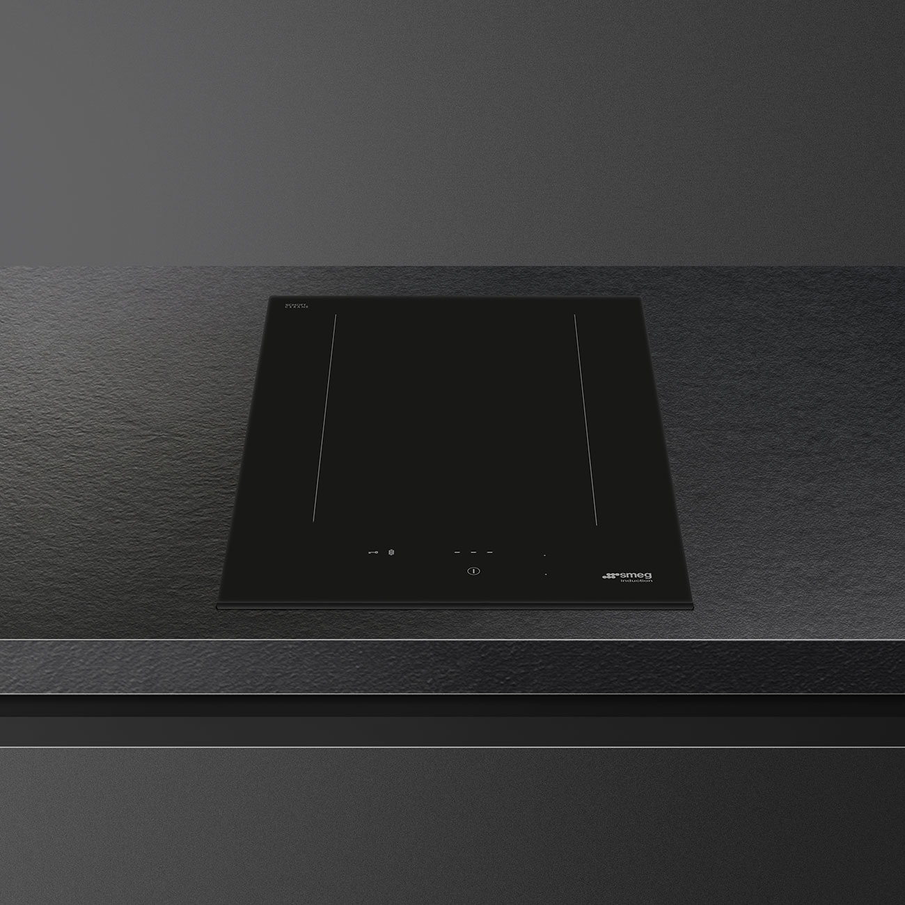 Un piano cottura a induzione Smeg nero con una singola zona di cottura, posizionato su un piano di lavoro scuro.