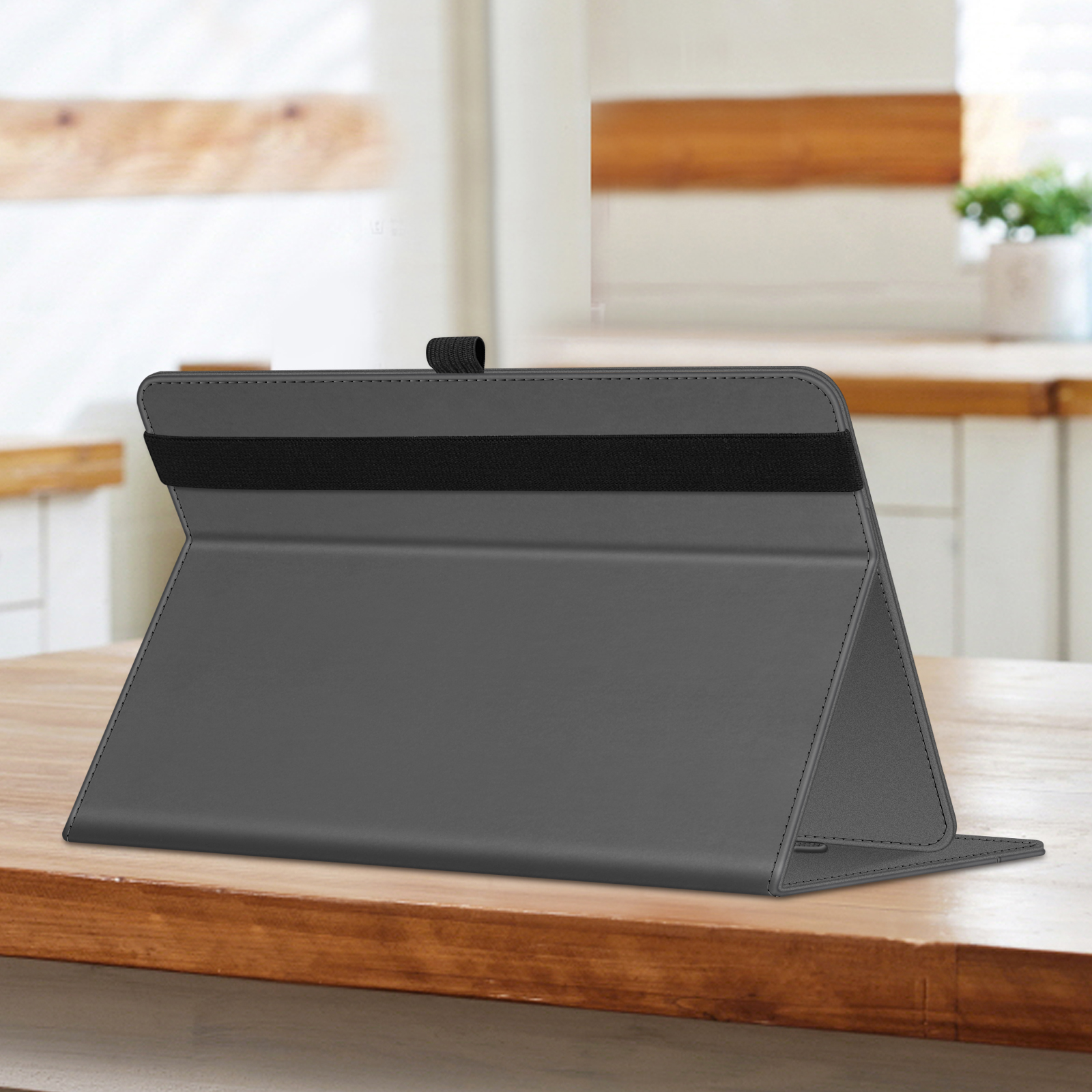 Eine graue Tablet-Hülle ist auf einem Holztisch vor einer weißen Küche geöffnet. Ein schwarzes Gummiband ist sichtbar.