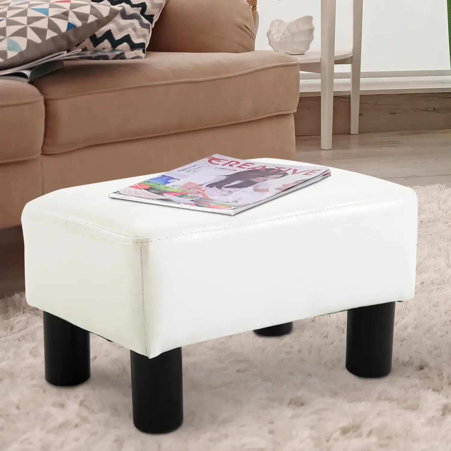 Weißer Hocker mit schwarzen Beinen. Eine Zeitschrift liegt darauf. Der Hintergrund zeigt ein Sofa.