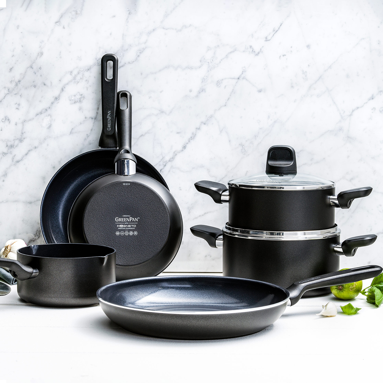 Schwarzes Kochgeschirr-Set auf weißer Oberfläche. Enthält Pfannen, Töpfe und eine Bratpfanne.