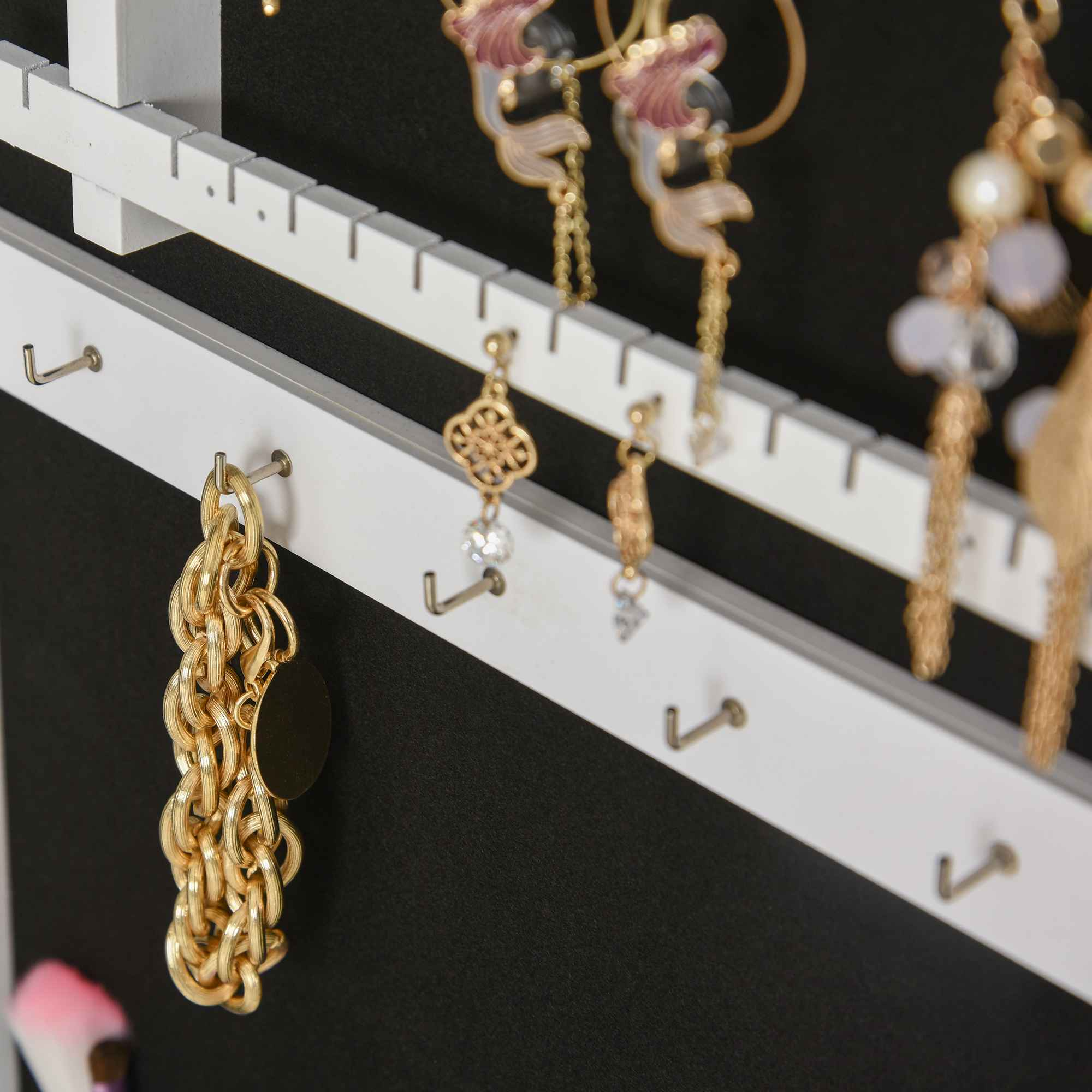 Eine Schmuckausstellung, die an einem weißen Gestell hängt. Verschiedene Ohrringe und eine goldene Kette sind sichtbar.