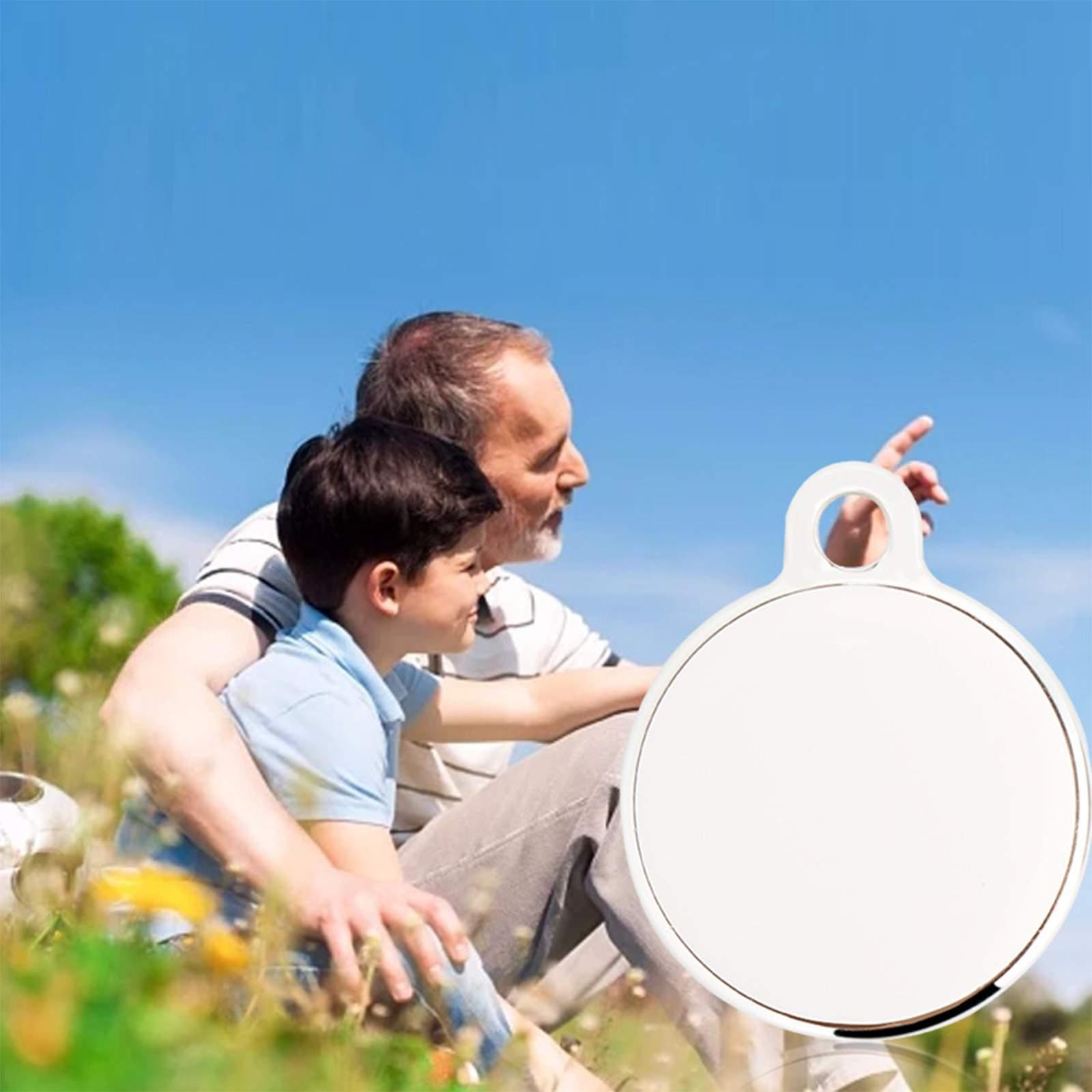 Ein Mann und ein Junge sitzen im Gras und schauen nach oben. Ein weißer runder Anhänger im Vordergrund.