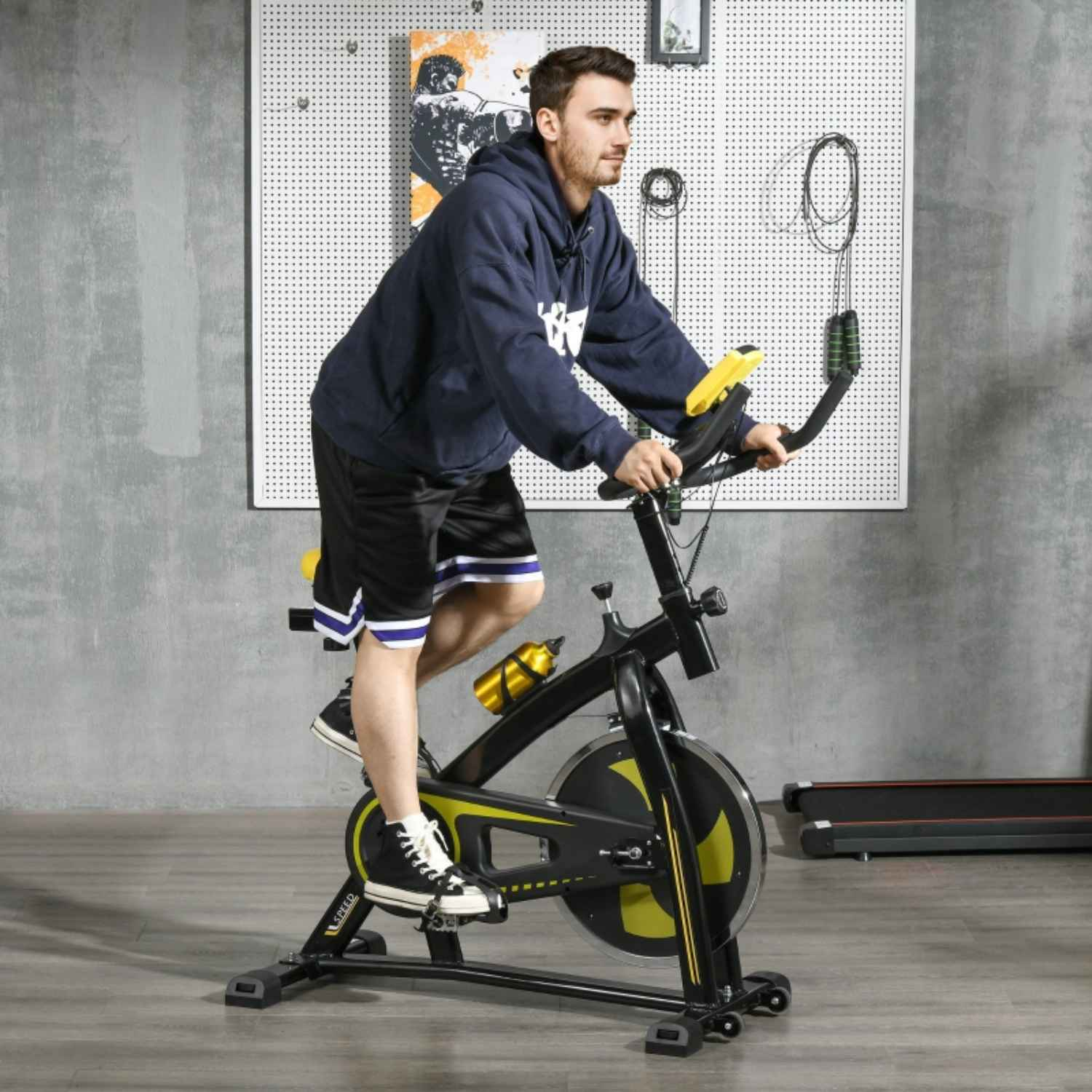 Mann auf einem schwarzen Heimtrainer in einem Heim-Fitnessstudio, mit blauem Hoodie.