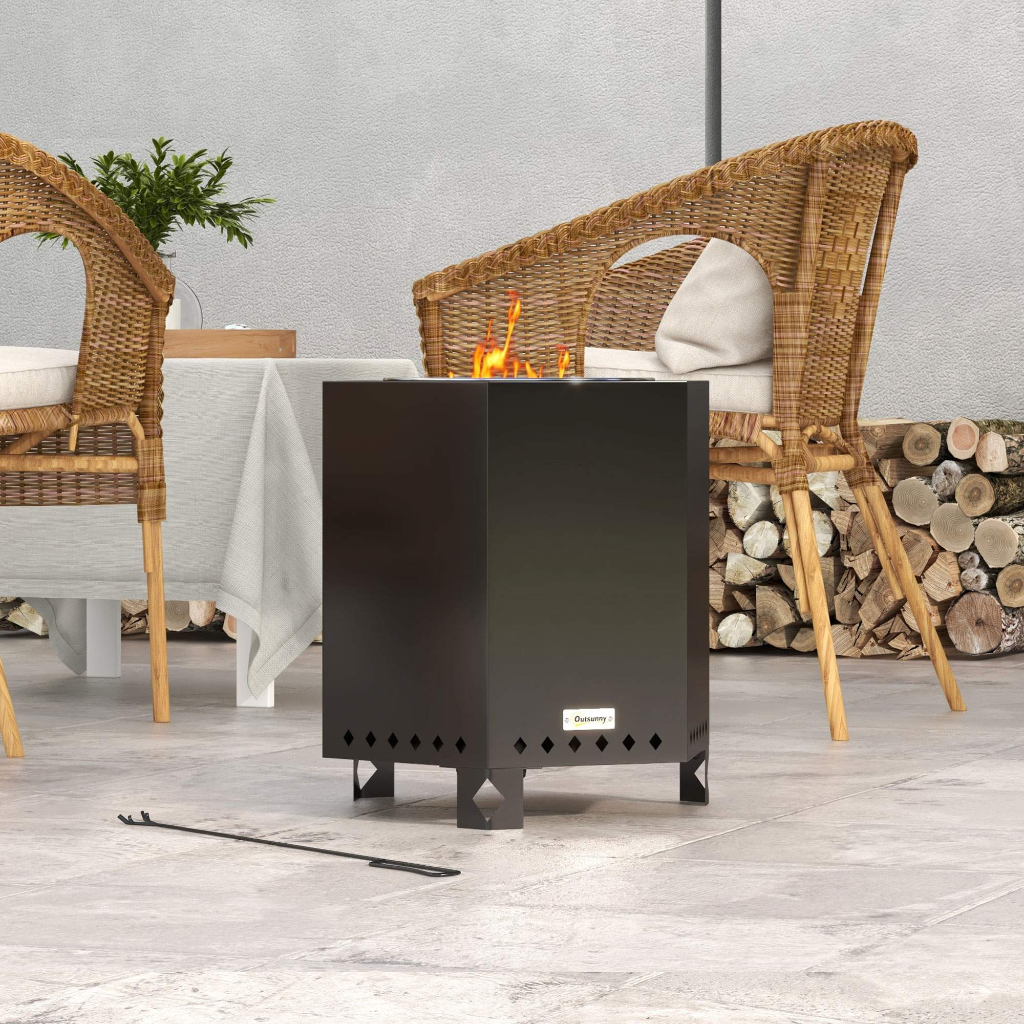 Schwarze Feuerstelle im Freien mit Feuer. Zwei Korbstühle, Tisch mit Tuch.