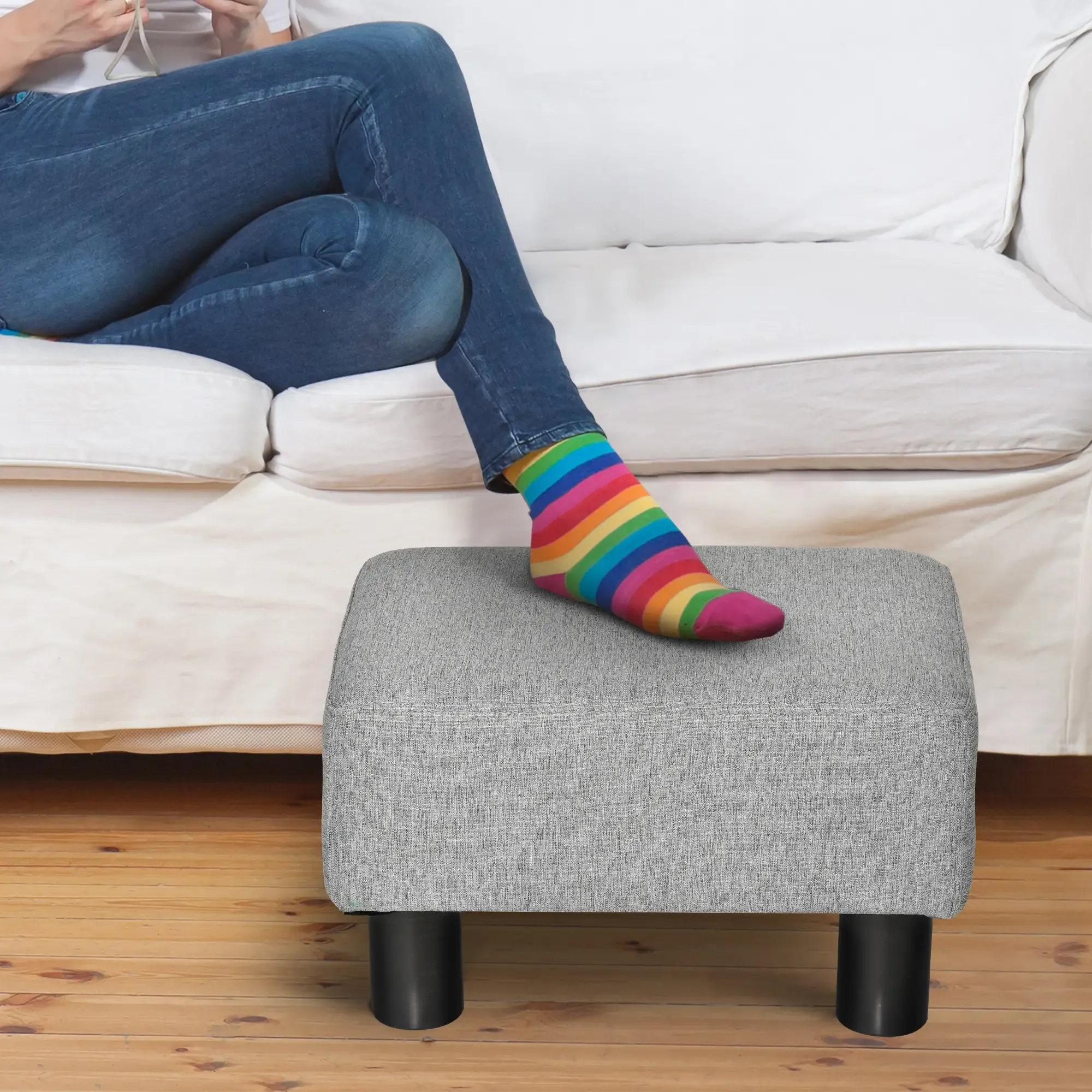 Person mit Regenbogensocken auf grauem Hocker. Sofa im Hintergrund.