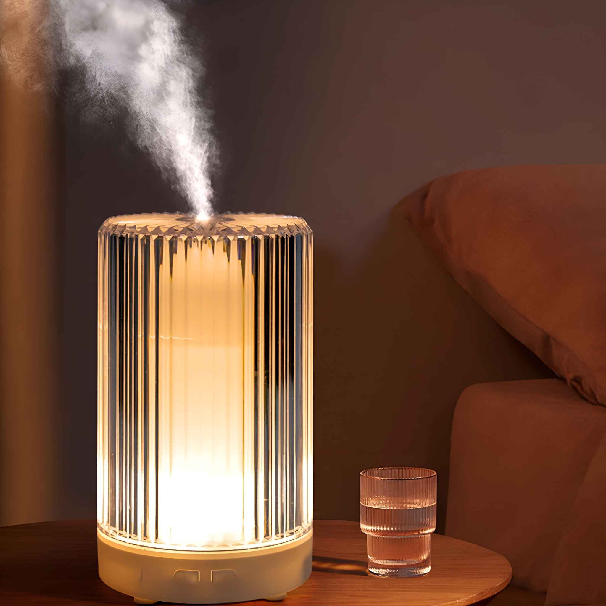 Ein Aromadiffusor, der Dampf abgibt, neben einem Glas Wasser und einem Sofa.