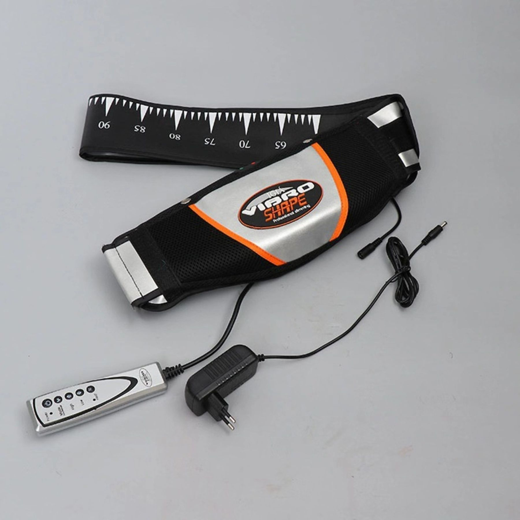 Ein Vibrationsgürtel, Fernbedienung, Netzteil und Ladekabel auf einer hellgrauen Oberfläche.