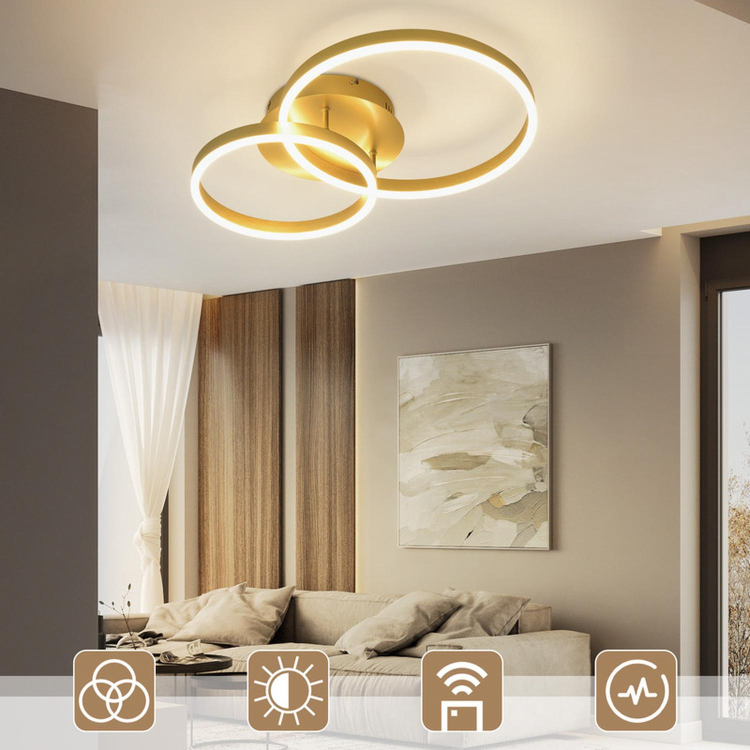 Lampada da soffitto dorata moderna con tre anelli collegati. Lo sfondo presenta un muro, arte e un divano.