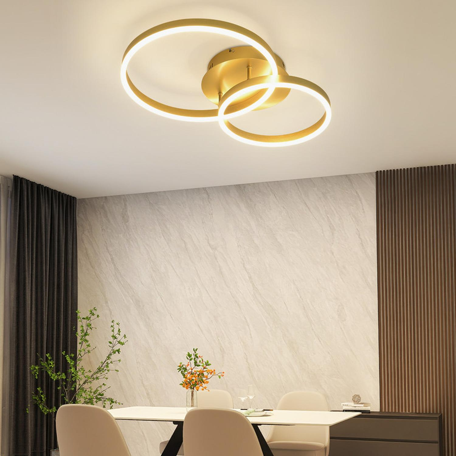 Una lampada da soffitto dorata con due forme circolari, sopra un tavolo da pranzo.