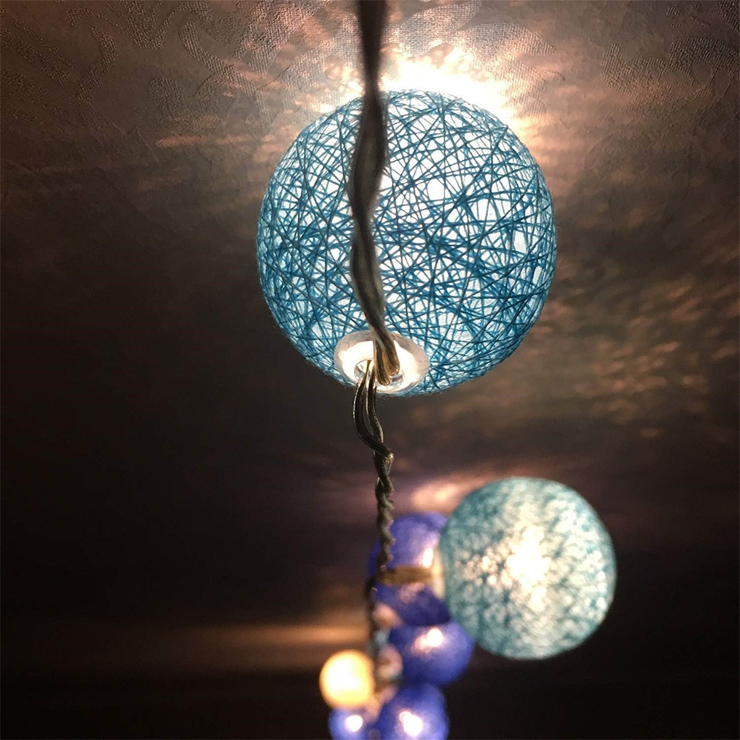 Nahaufnahme einer Lichterkette mit blauen Kugeln. Eine Leuchte leuchtet hell.