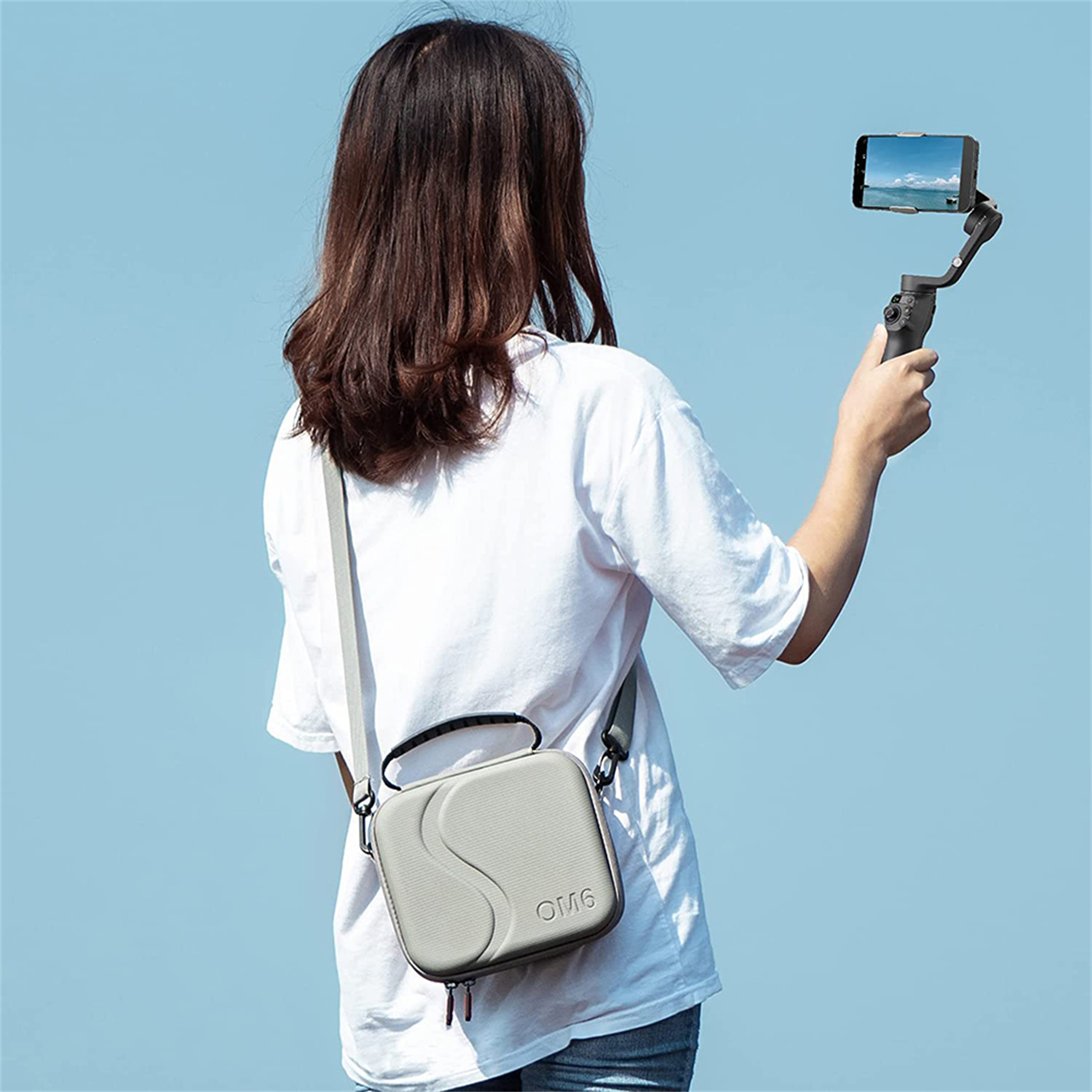 Eine Frau, die ein Telefon an einem Gimbal hält, mit einer grauen Tragetasche über der Schulter.