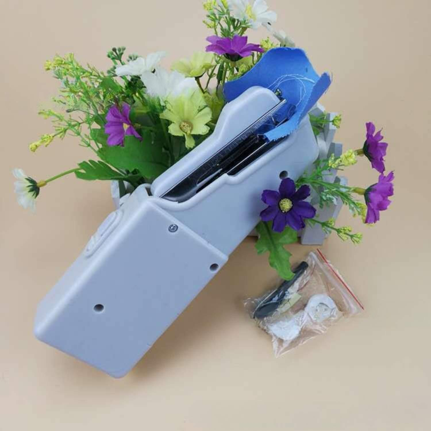 Eine graue Handnähmaschine mit einem blauen Stoff, der genäht wird. Blumen sind im Hintergrund.