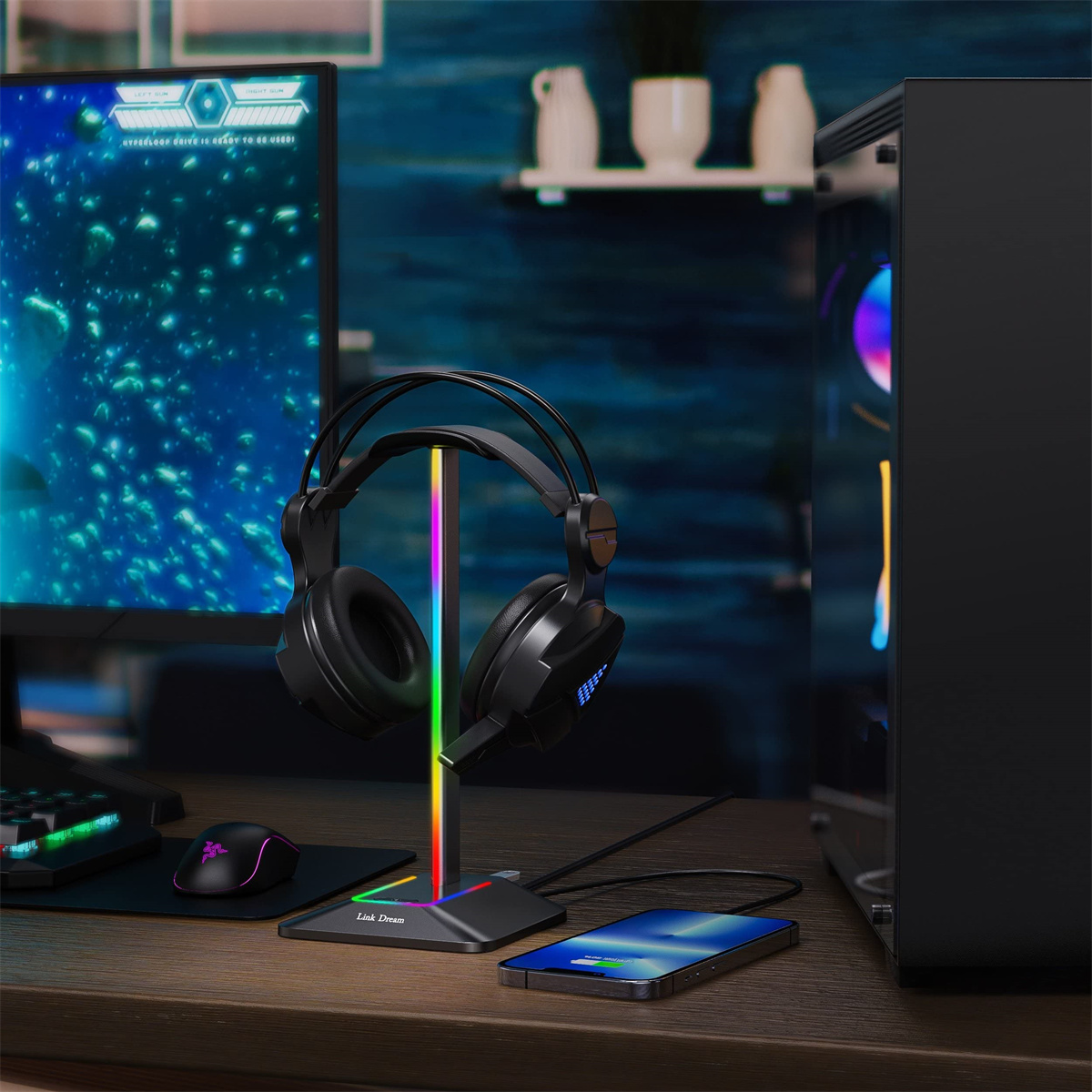 Ein Schreibtisch-Setup mit einem Kopfhörerständer mit Regenbogenbeleuchtung, Kopfhörern, einem Monitor und einem Telefon.