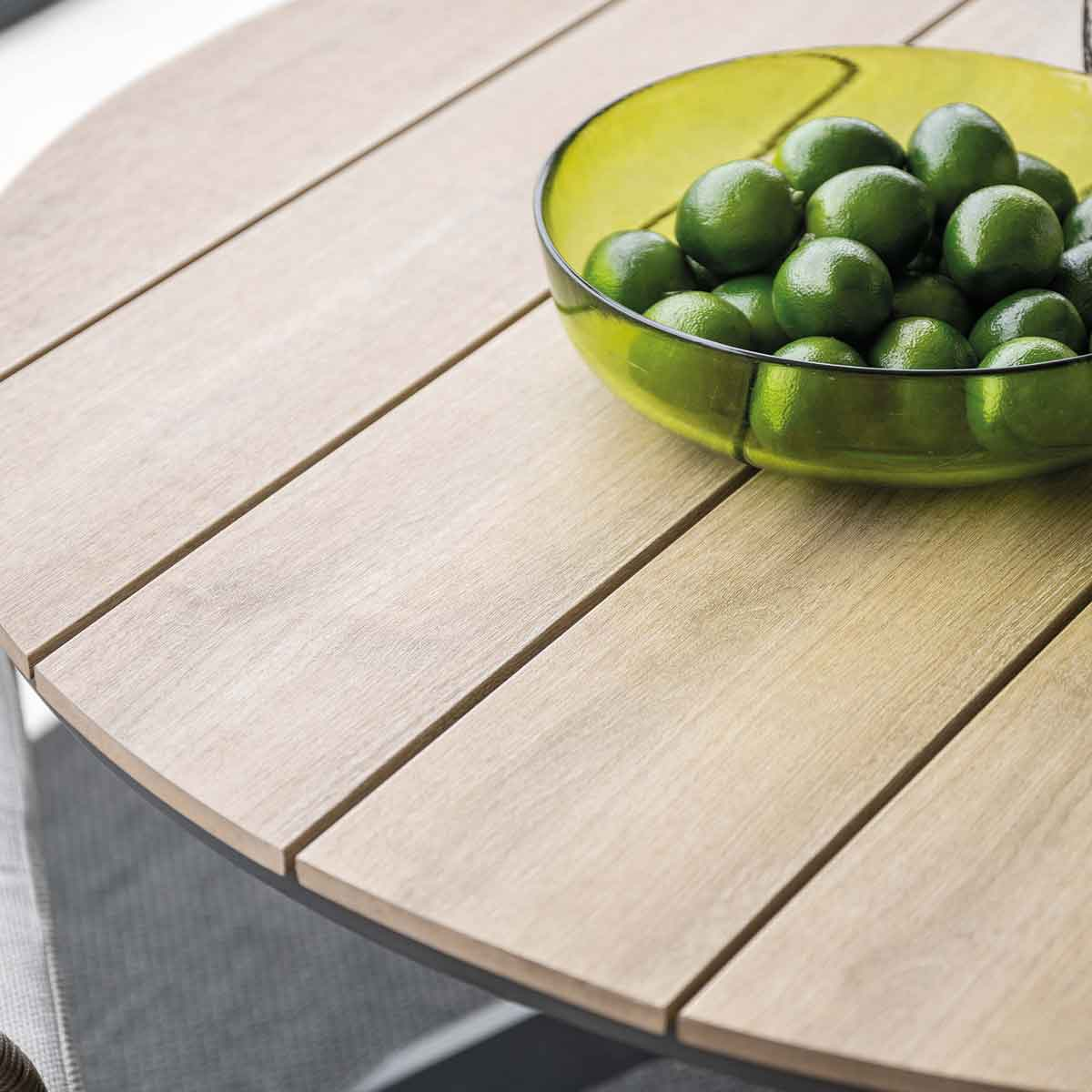 A table made of wood with a green bowl filled with limes on top.