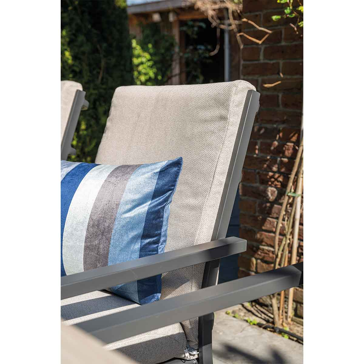 Close-up of a chair with a cushion and a blue and gray striped pillow in an outdoor setting.