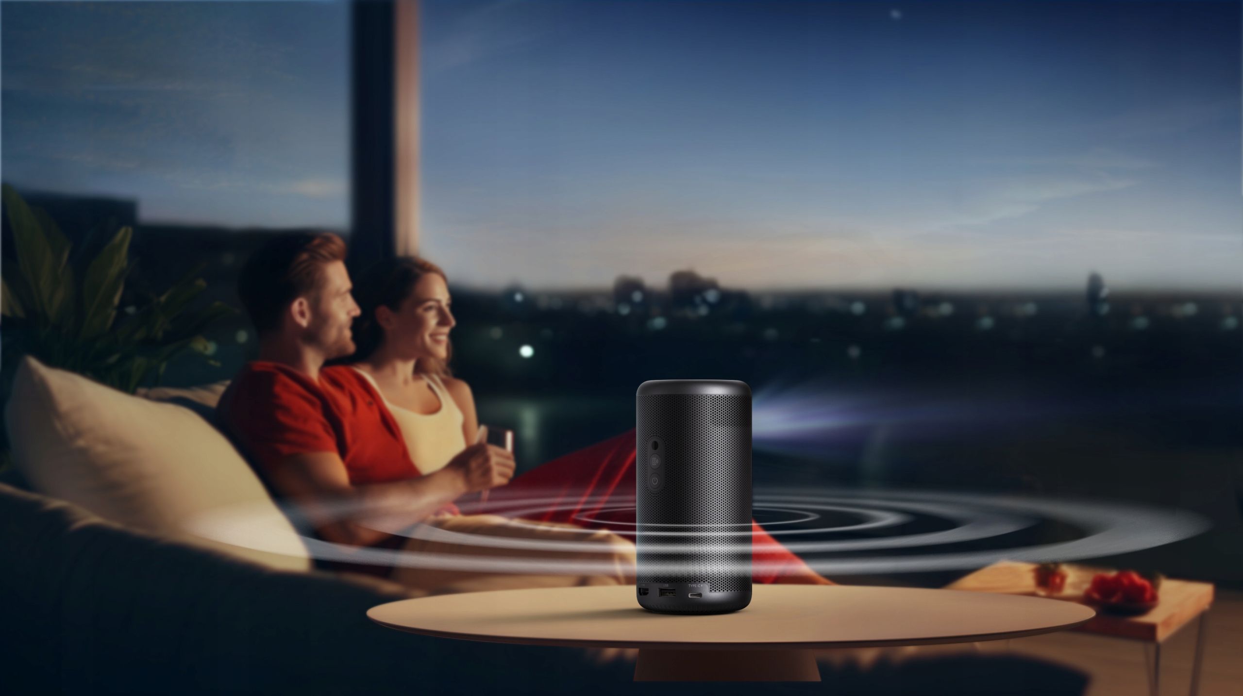 Para siedzi na kanapie, patrząc w stronę głośnika na stole. Widoczne nocne niebo.