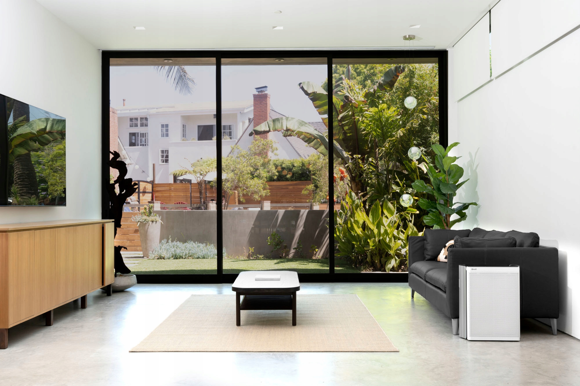 Nowoczesne wnętrze z dużymi oknami, sofą, stolikiem kawowym i białym oczyszczaczem powietrza.