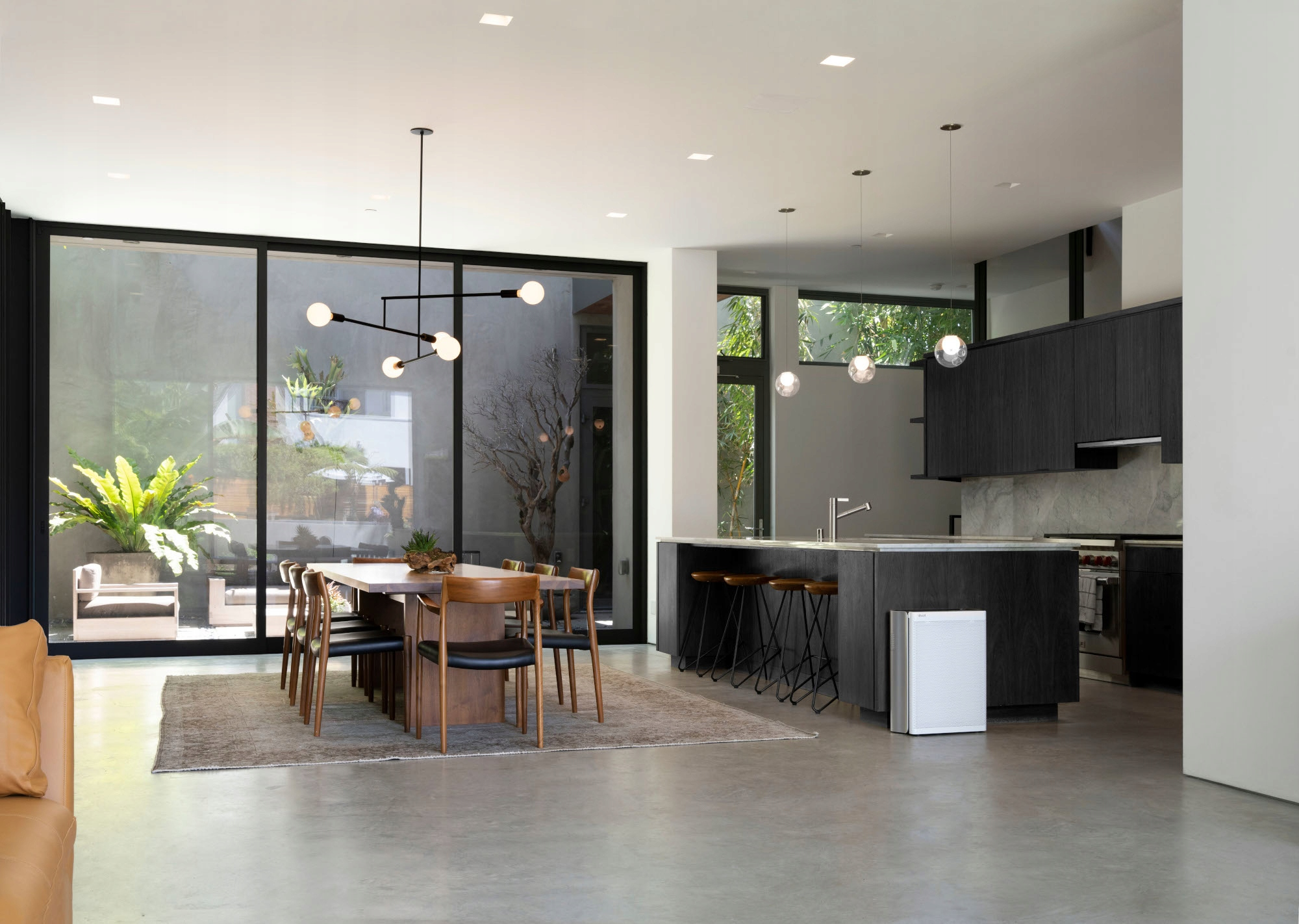 Przestronne wnętrze ze stołem jadalnym, krzesłami, otwartą kuchnią i białym oczyszczaczem powietrza.