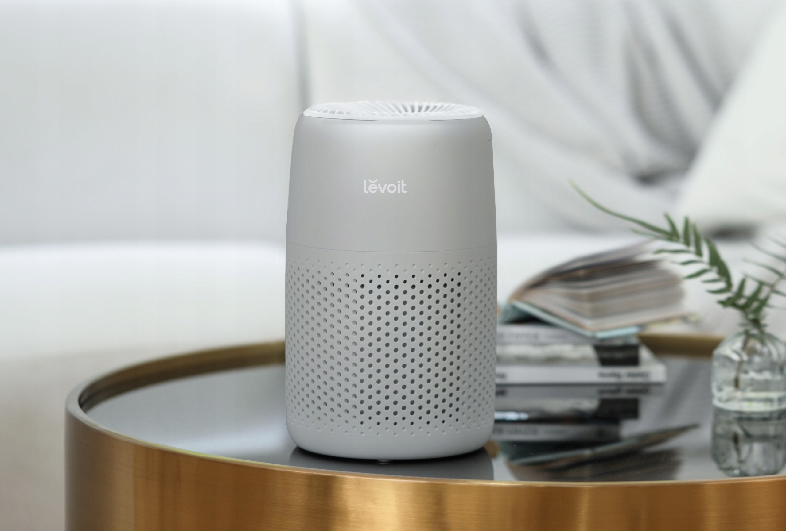 Szary oczyszczacz powietrza na złotym stole, rozmyte tło kanapy i okna.