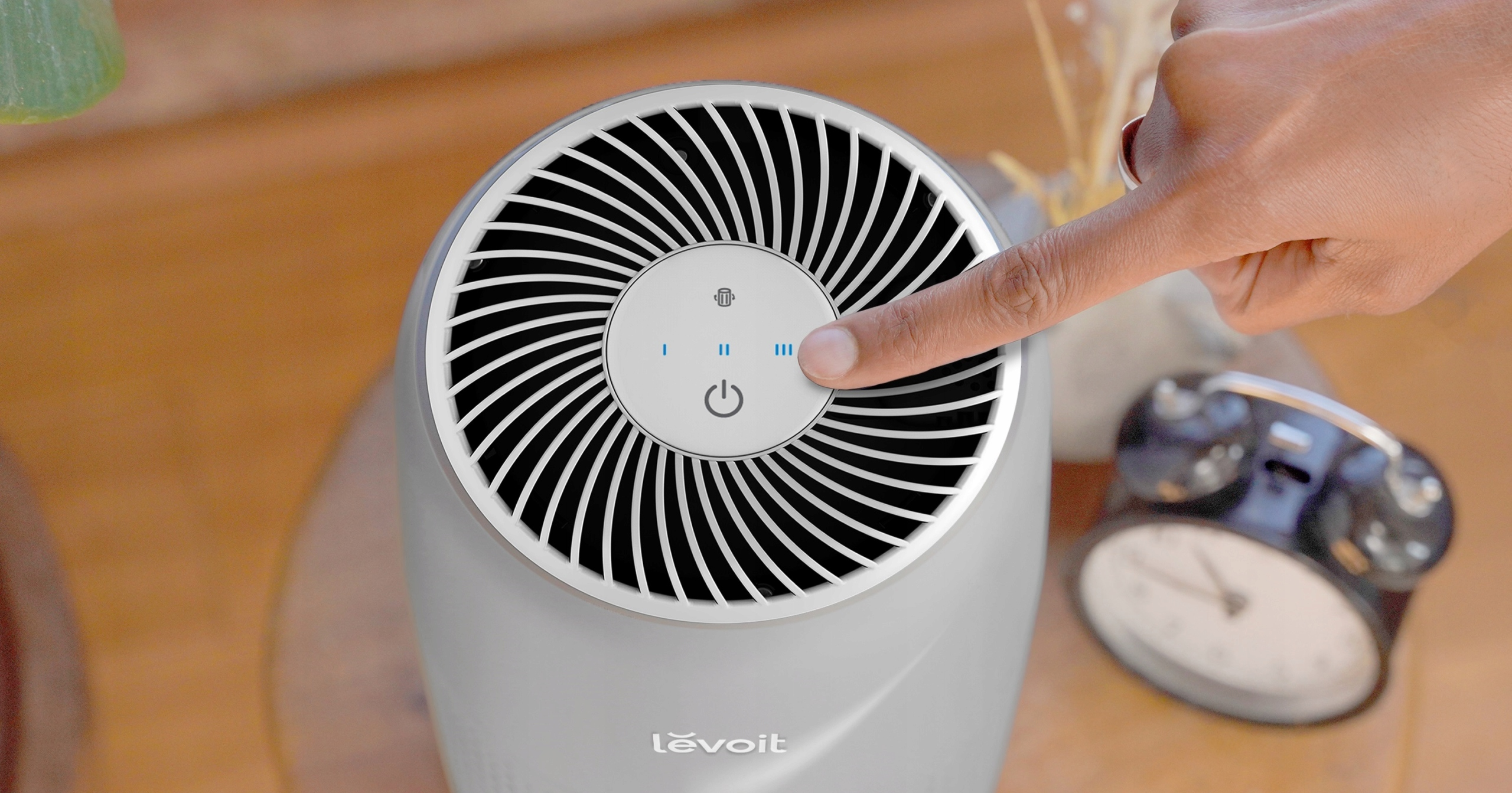 Ręka naciskająca przycisk zasilania na szarym oczyszczaczu powietrza z panelem sterowania.