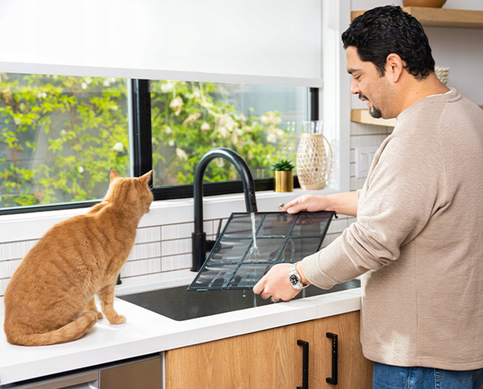Mężczyzna myje filtr powietrza w zlewie, z kotem obserwującym z bliska.