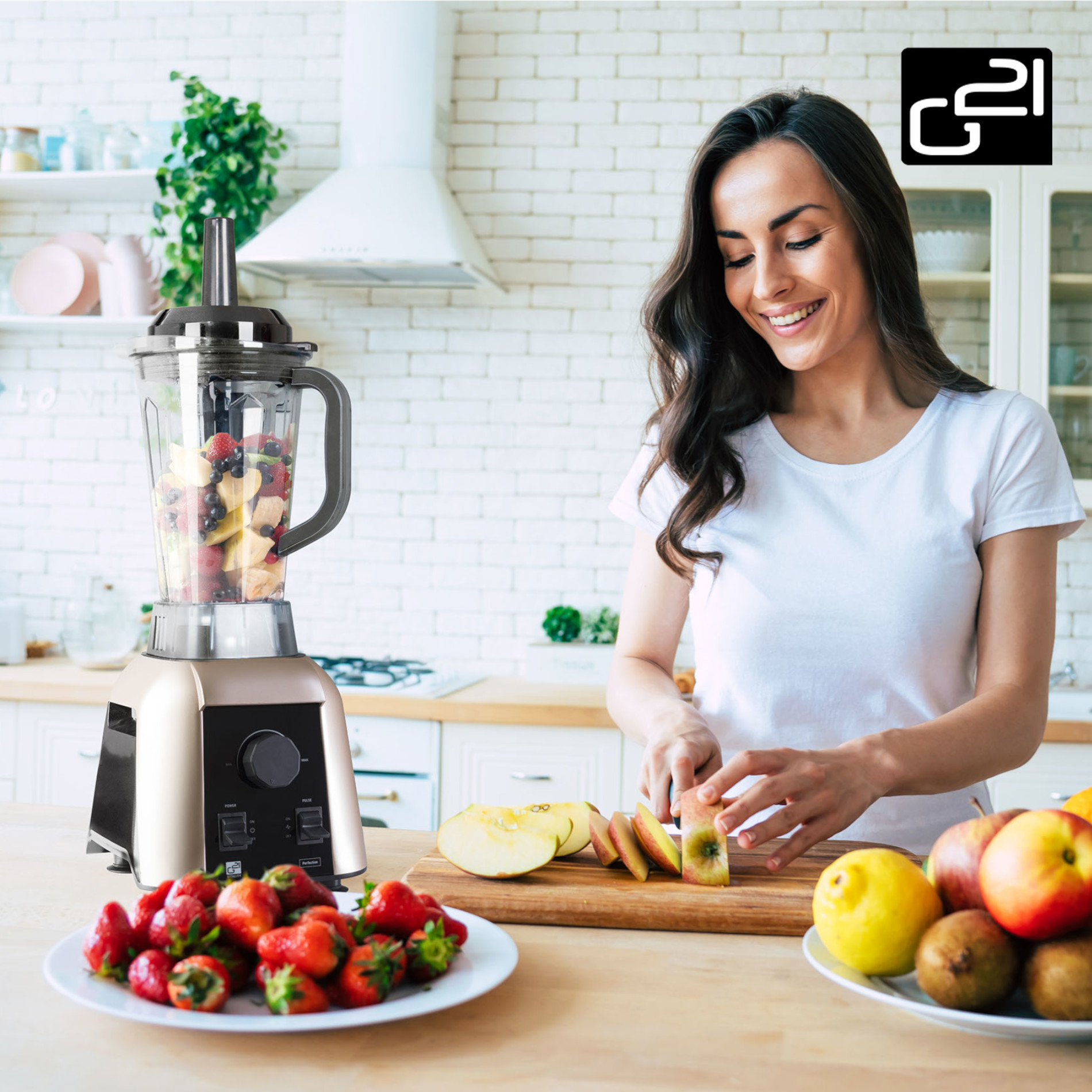Kobieta kroi owoce obok blendera wypełnionego owocami. Na talerzu i stole są owoce.