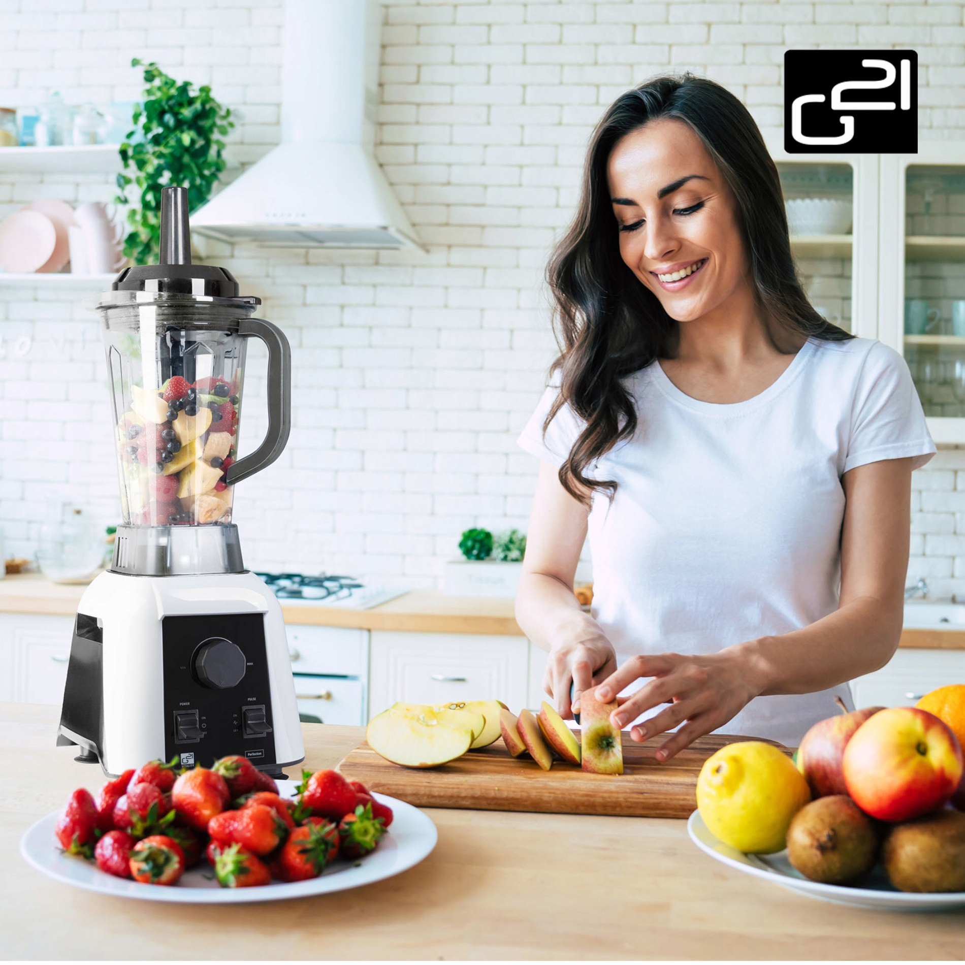 Kobieta krojąca owoce obok blendera wypełnionego owocami, na kuchennym blacie z jedzeniem.