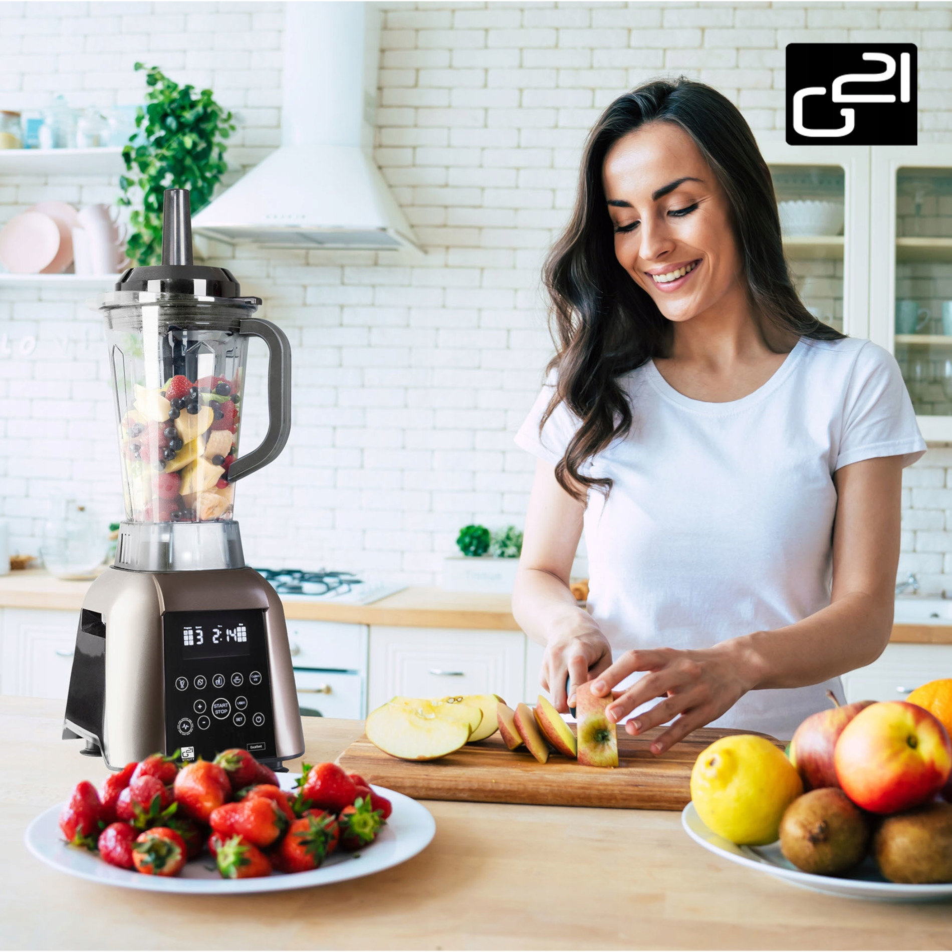 Kobieta przygotowująca koktajl. Blender z owocami. Talerz truskawek i jabłek na blacie.