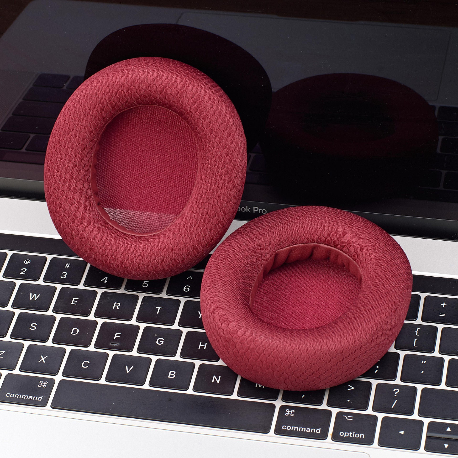 Zwei weinrote Ohrpolster liegen auf einer Laptop-Tastatur. Sie sind kreisförmig mit einer zentralen Öffnung.