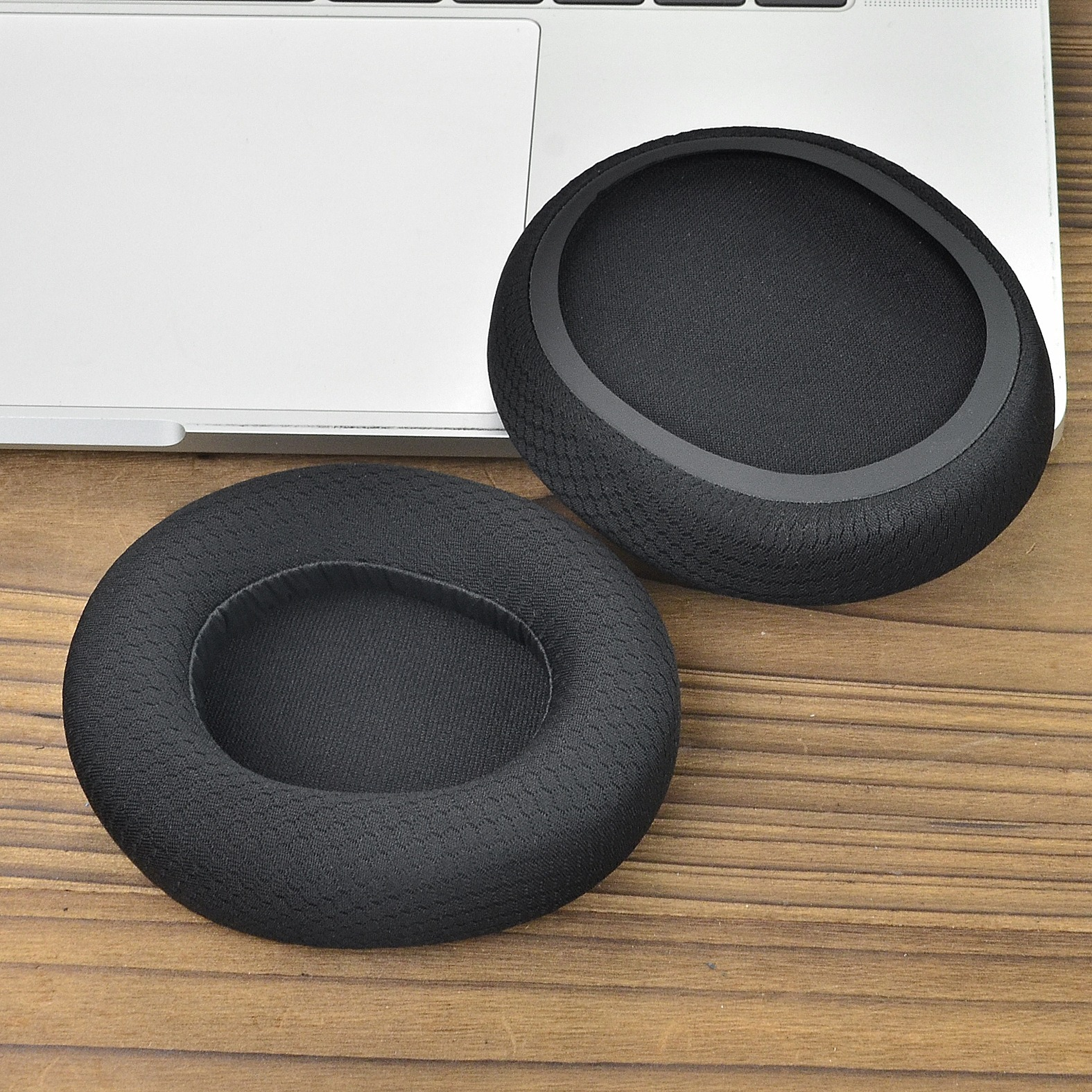 Due cuscinetti auricolari neri sono su una tastiera di un laptop. Hanno un interno in rete nera e una superficie scura e strutturata.