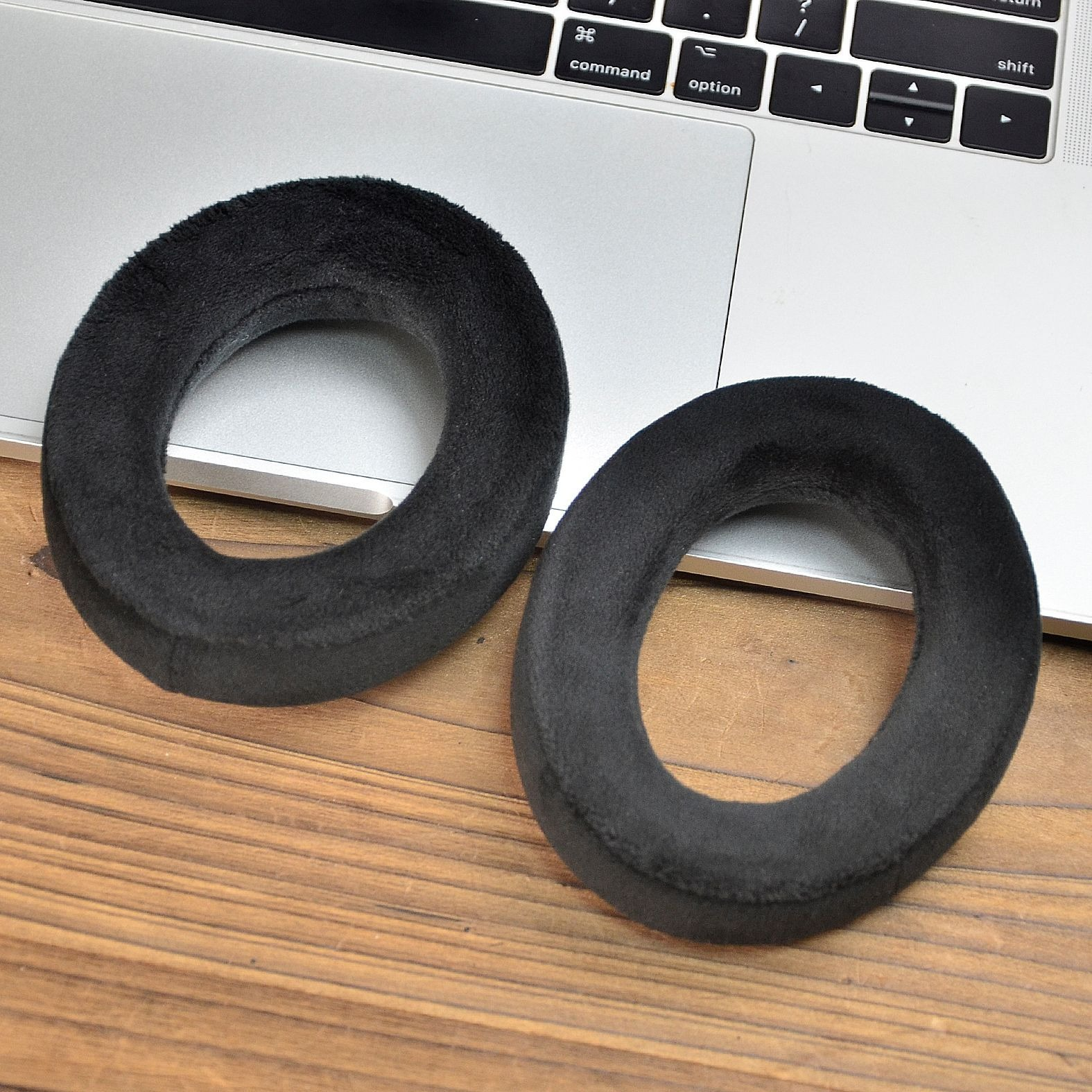 Due cuscinetti auricolari neri e rotondi sono posizionati su una superficie di legno. Hanno una superficie morbida e strutturata.
